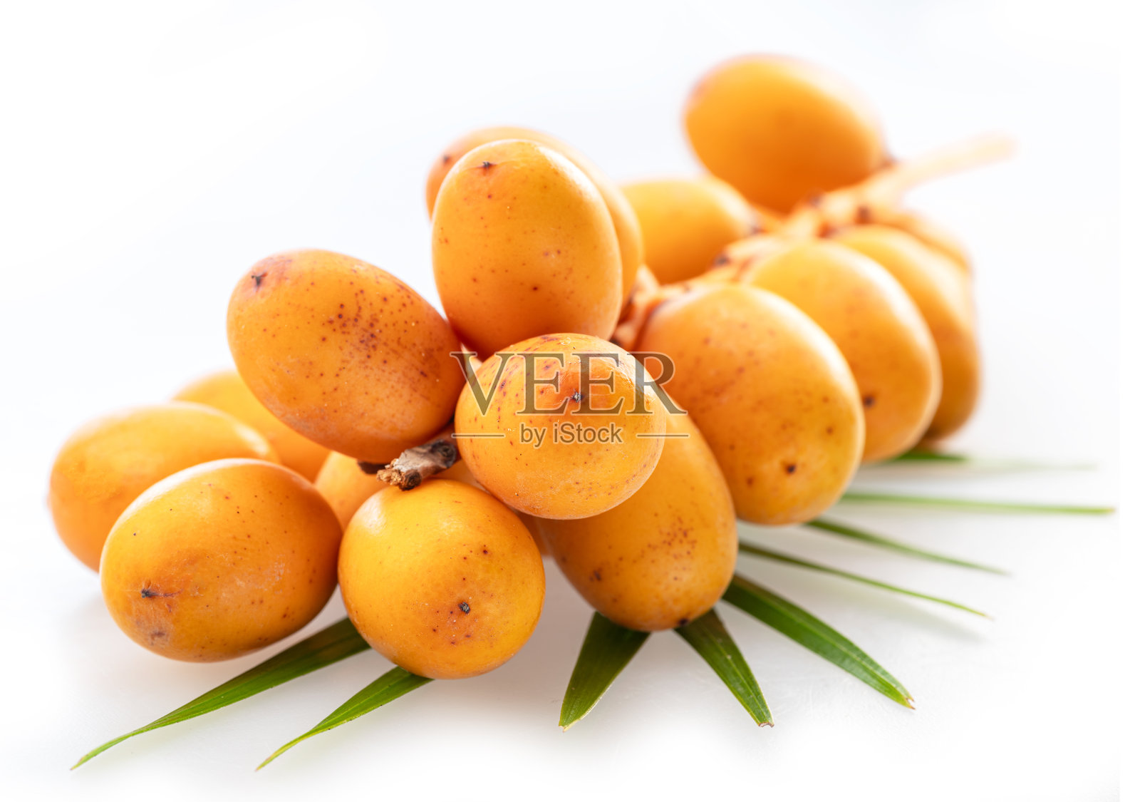 一簇新鲜的黄色枣子,或称为椰枣果,躺在棕榈叶上,背景为白色。文件包含抠图路径。照片摄影图片