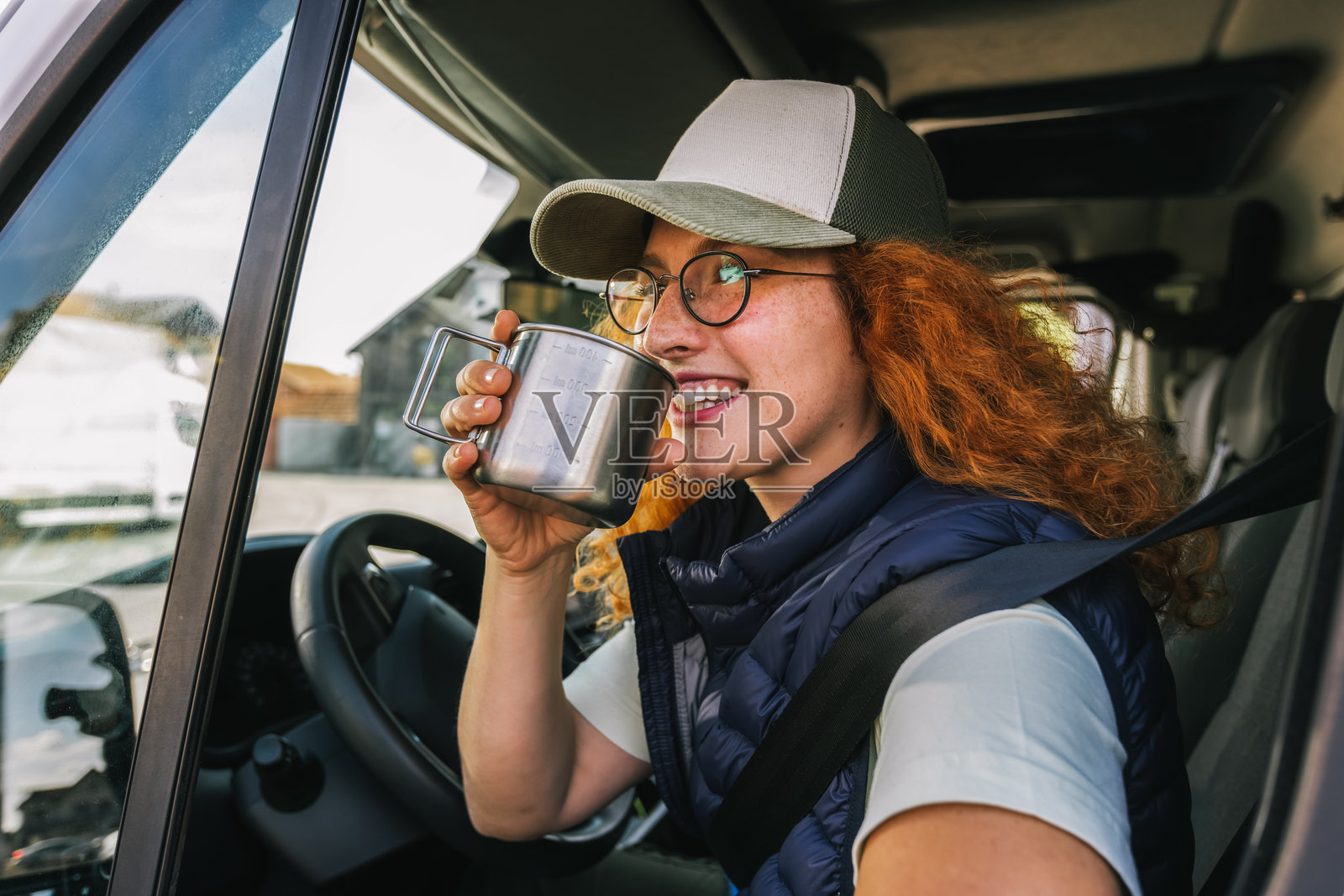 年轻的红发女性驾驶长途车辆,喝着咖啡以补充能量。照片摄影图片