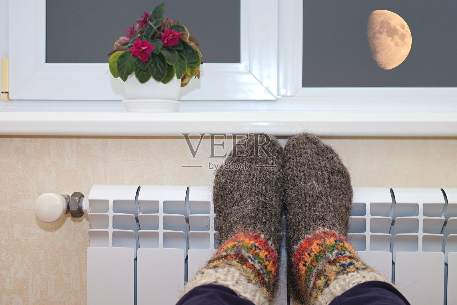 温暖的毛袜脚放在窗边的暖气片上,窗外是月光照耀的夜空。照片摄影图片