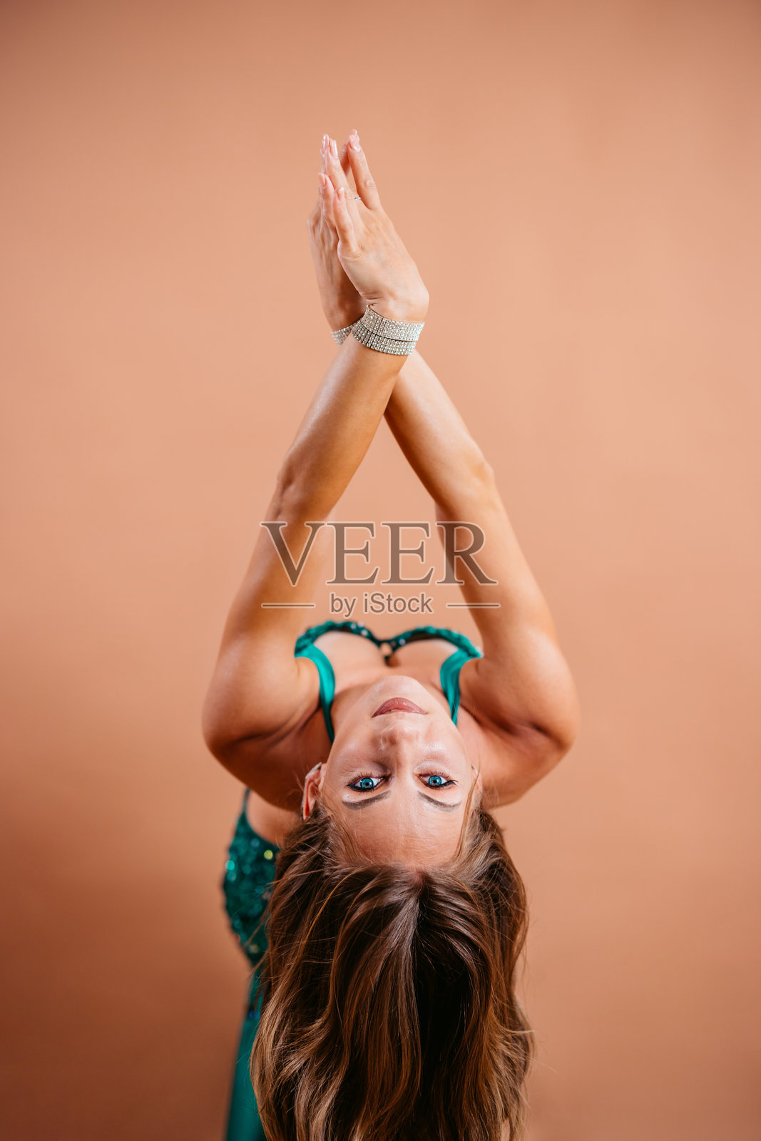 身穿翡翠色服装的年轻女性在米色背景下表演肚皮舞照片摄影图片