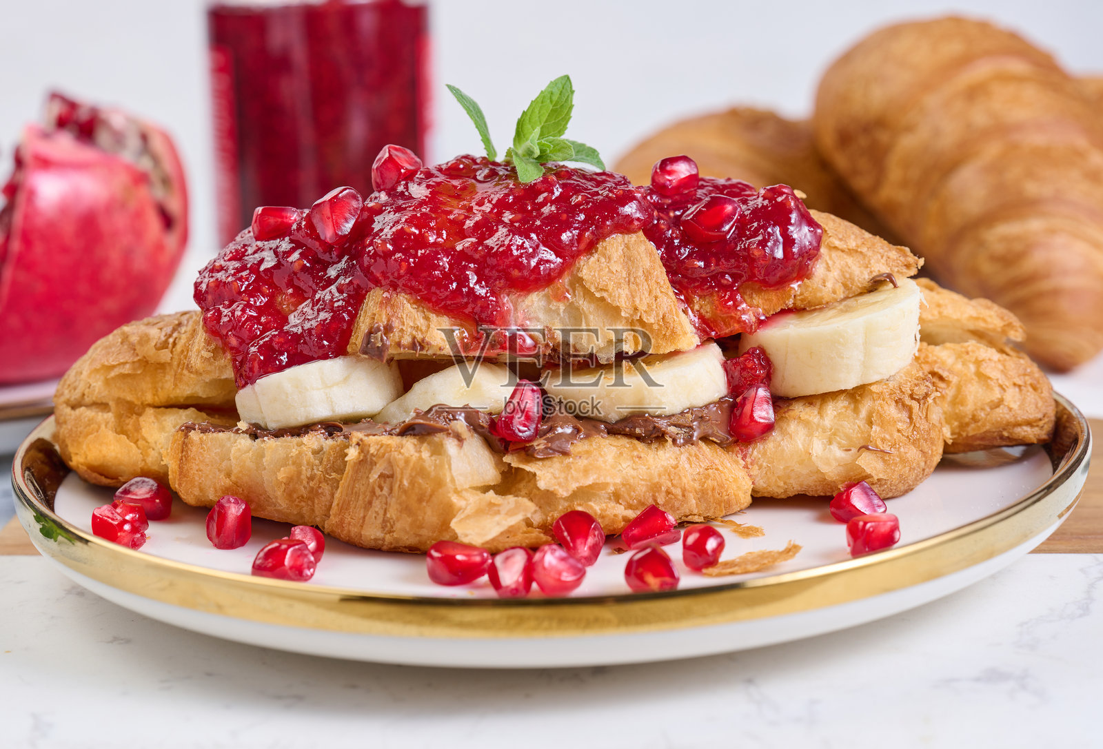 圆白盘中的可颂,配有香蕉块、巧克力酱和石榴籽照片摄影图片