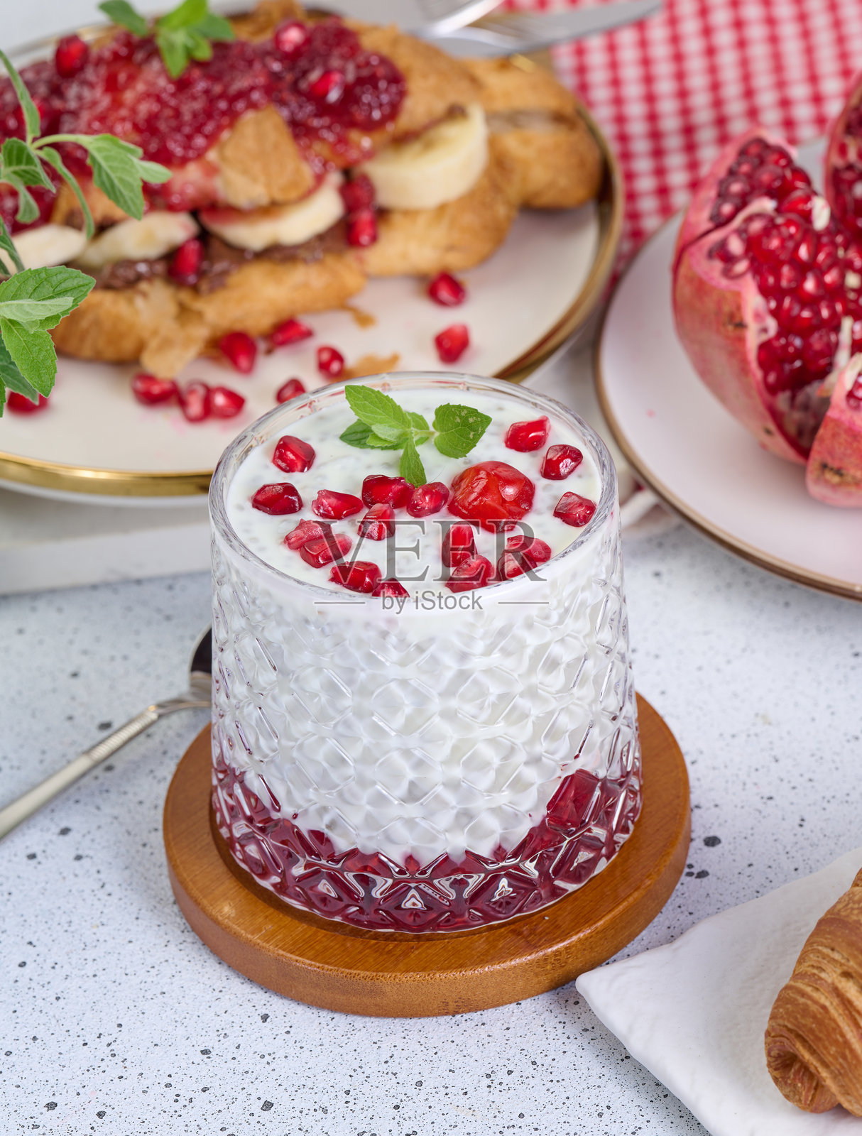 桌子上放着一杯酸奶,里面有奇亚籽和石榴籽,还有一些烤好的可颂。照片摄影图片
