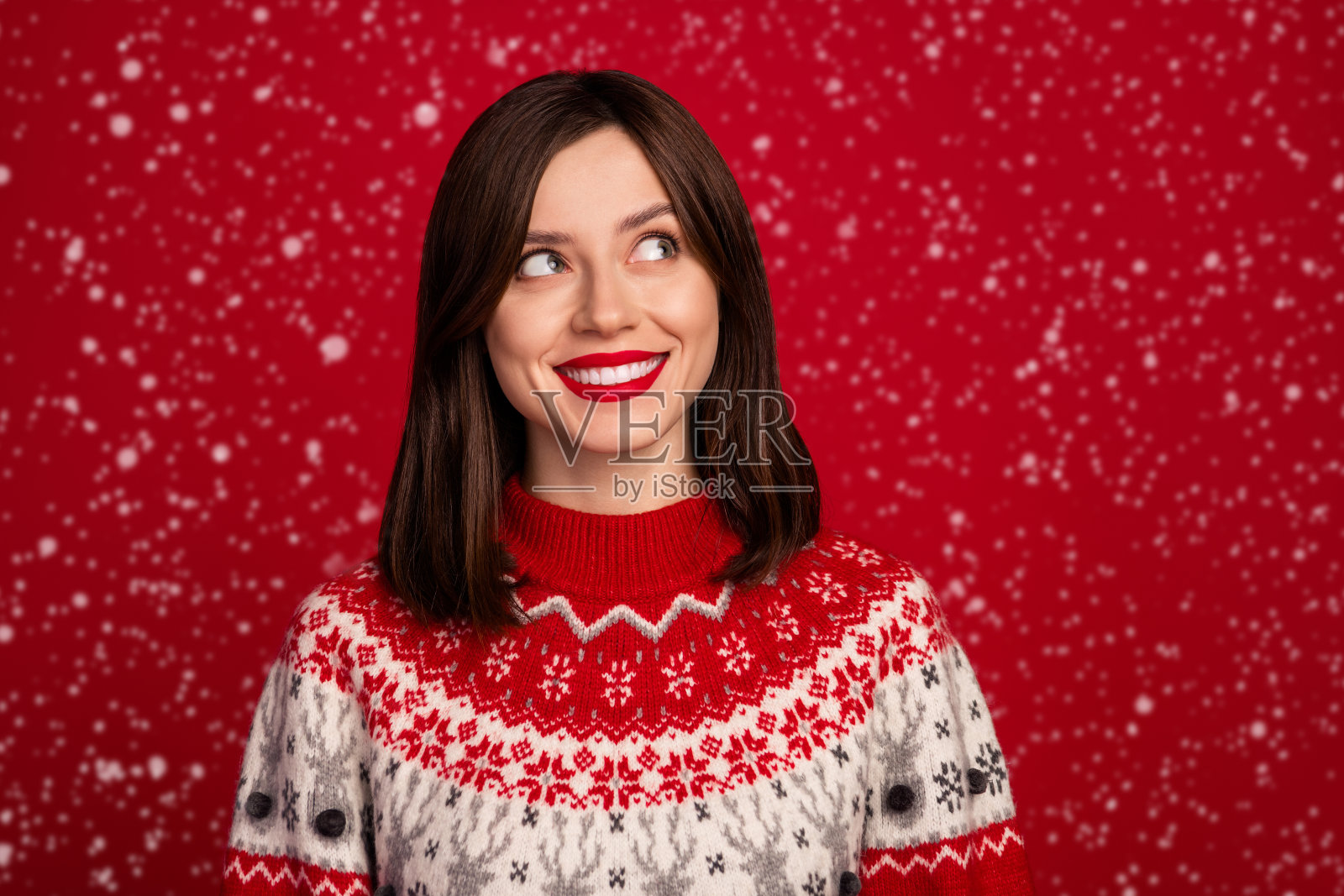 积极、快乐、可爱的乐观女性肖像,留着短发,穿着红色毛衣,目光投向空旷的空间,背景为红色。照片摄影图片