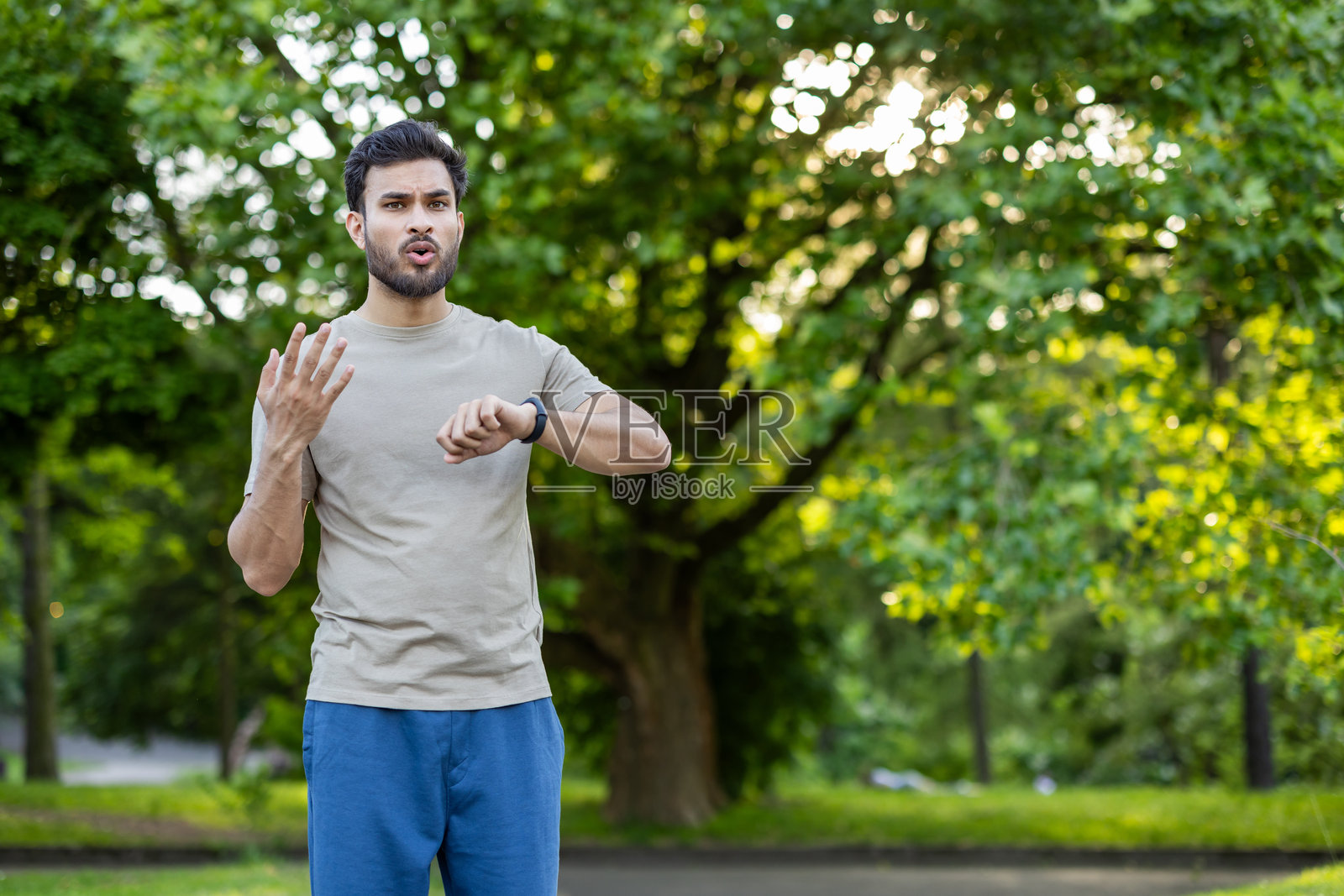 公园里的一名男子在阳光明媚的日子里查看健身手表,对锻炼后的结果表示不满。照片摄影图片
