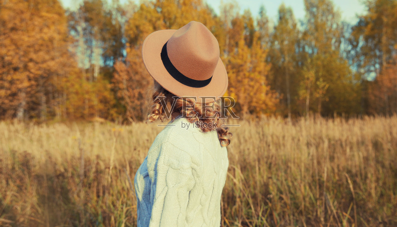 美丽的女人戴着帽子,在秋天的公园里享受温暖的天气,背景是黄色的树叶和自然风光。照片摄影图片