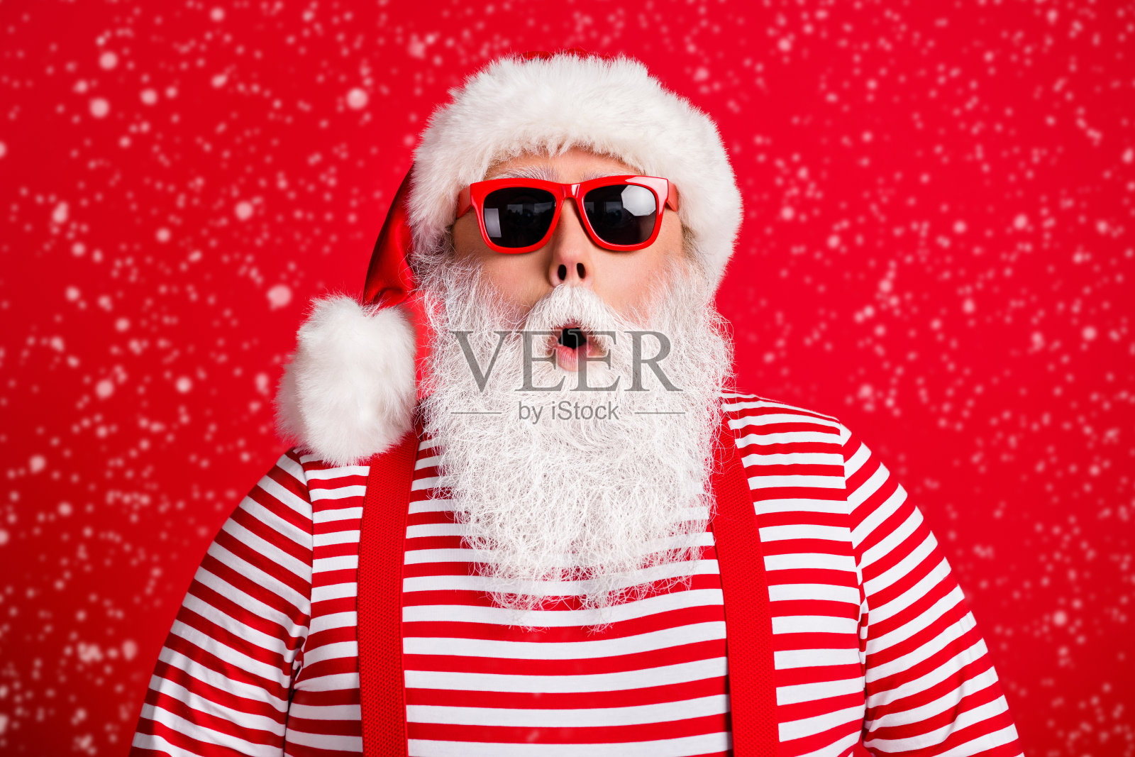 特写肖像:一位英俊迷人的白发圣诞老人,惊讶而震惊,佩戴着太阳镜,背景为明亮鲜艳的红色,适合圣诞促销。照片摄影图片