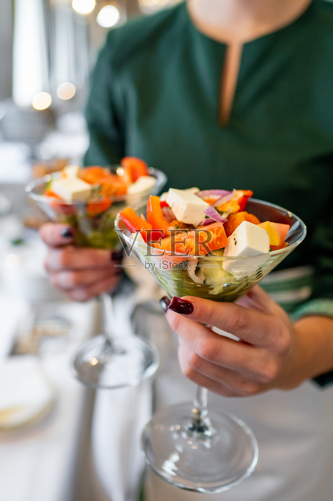 在社交聚会上,特写镜头展示双手捧着装满新鲜沙拉的玻璃碗,体现健康饮食。丰富多彩的蔬菜混合突显出营养丰富且色彩斑斓的餐食选择。照片摄影图片