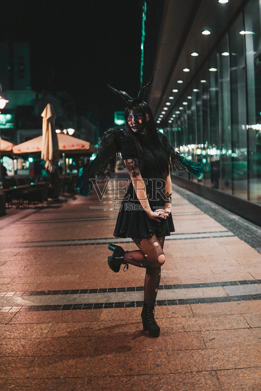 穿着可怕万圣节服装的女人,城市中的女巫,脸部彩绘面具和手臂上的纹身。照片摄影图片