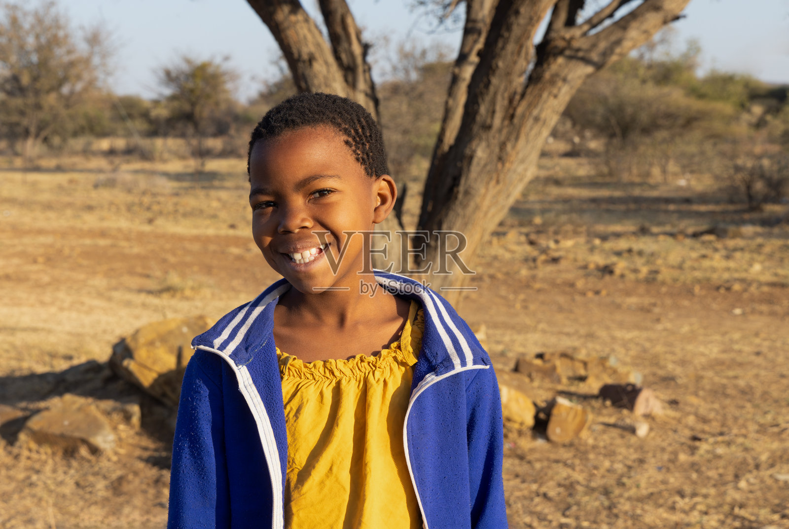 户外村庄中单独非洲儿童的肖像,背景有树木和灌木丛。照片摄影图片