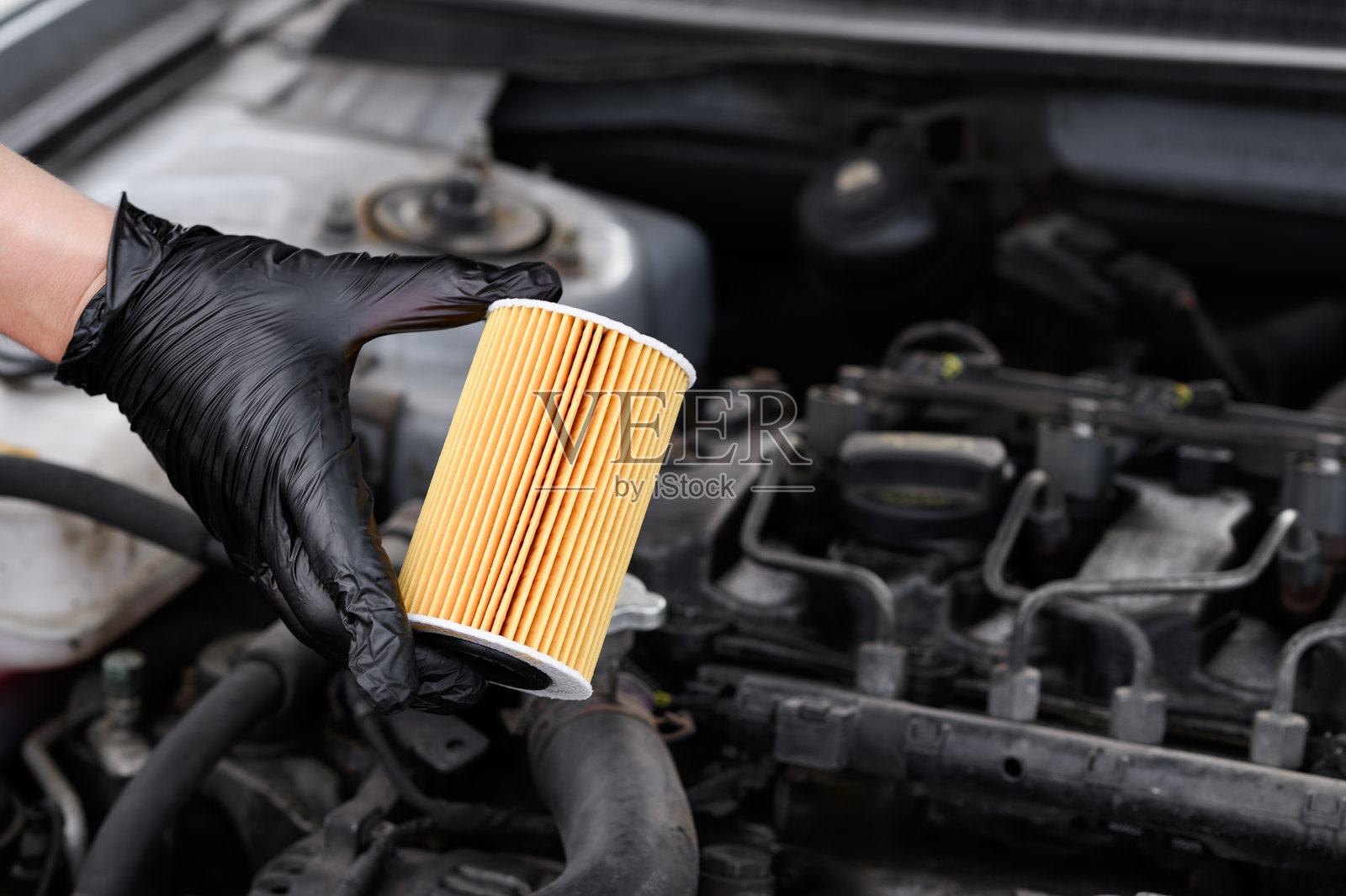 汽车修理工手持柴油车的机油滤清器,背景为发动机舱特写。汽车零件更换、换油和汽车机油滤清器的概念,汽车维护。照片摄影图片