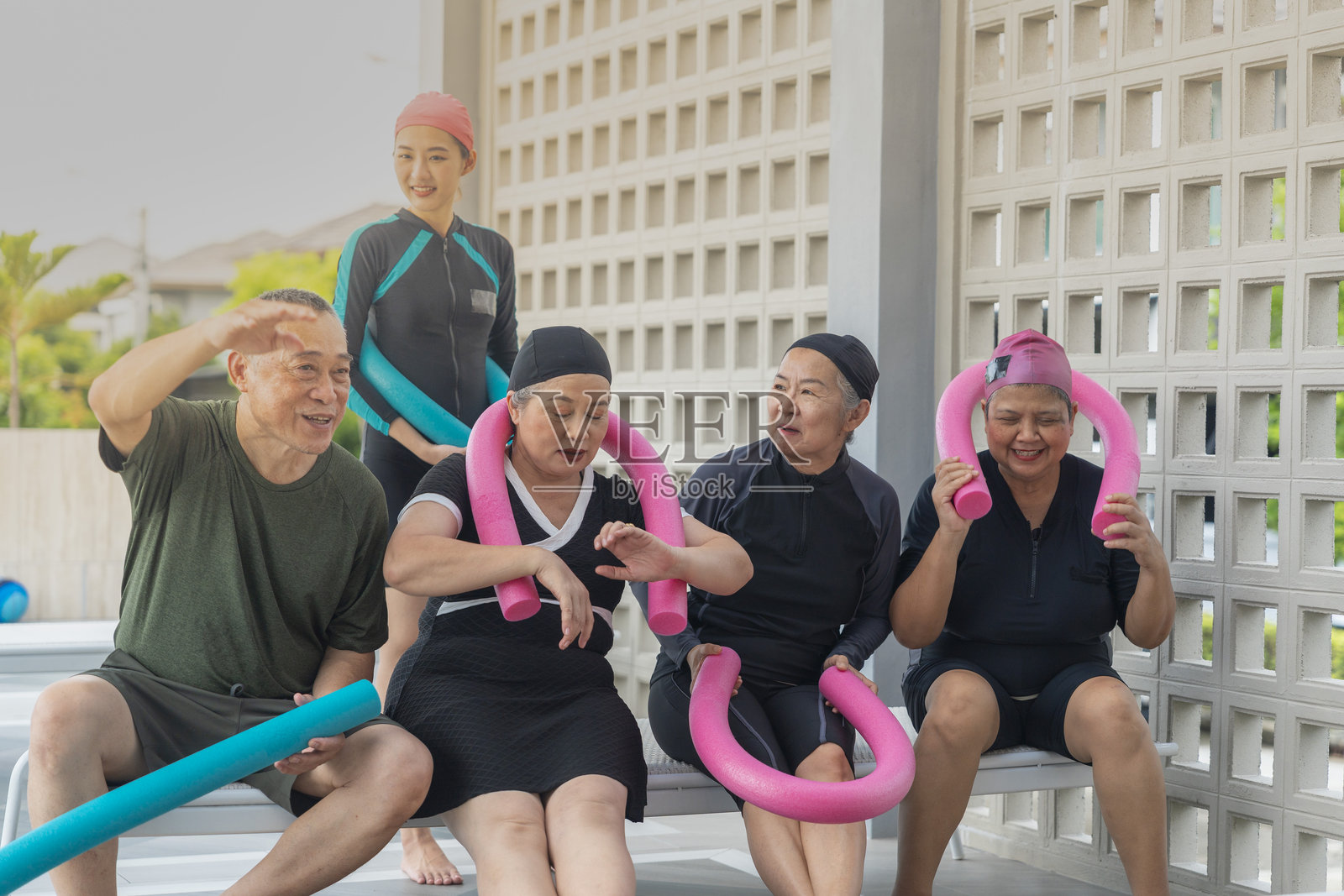 一群快乐的老年人在户外参加有趣的水中健身课程,使用五颜六色的泳池泡沫棒进行拉伸和平衡练习。他们积极参与健身活动,保持活力与健康。照片摄影图片