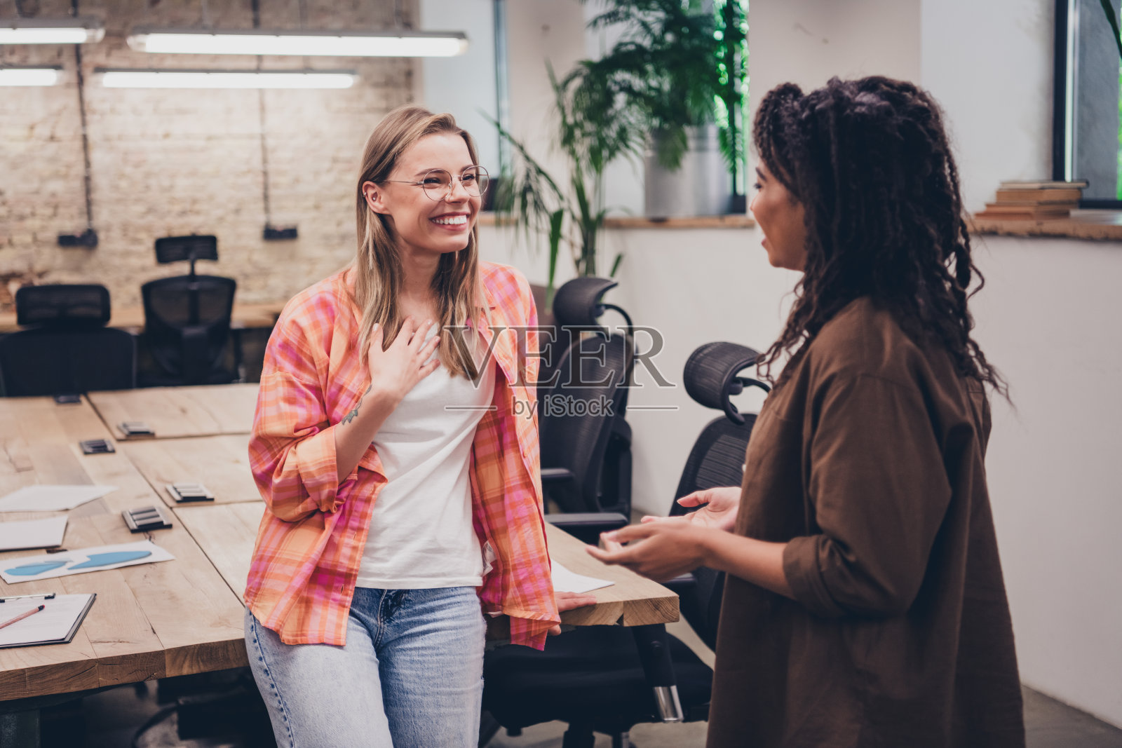 两位雄心勃勃的女商人在现代阁楼办公室内微笑交谈,共同工作。照片摄影图片
