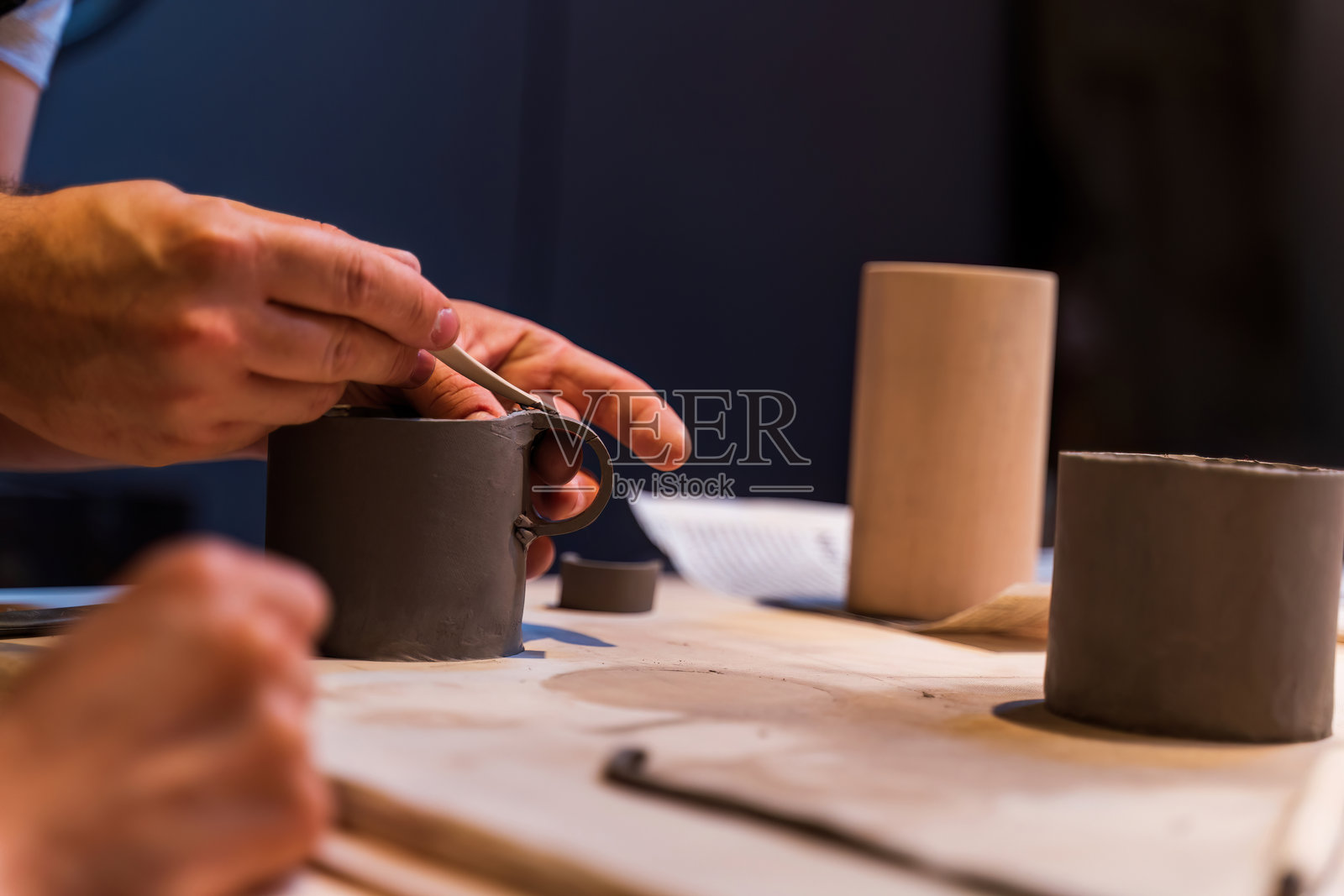 在温暖灯光的手工艺工作室中,特写镜头展示双手细致地用粘土制作陶瓷杯。照片摄影图片