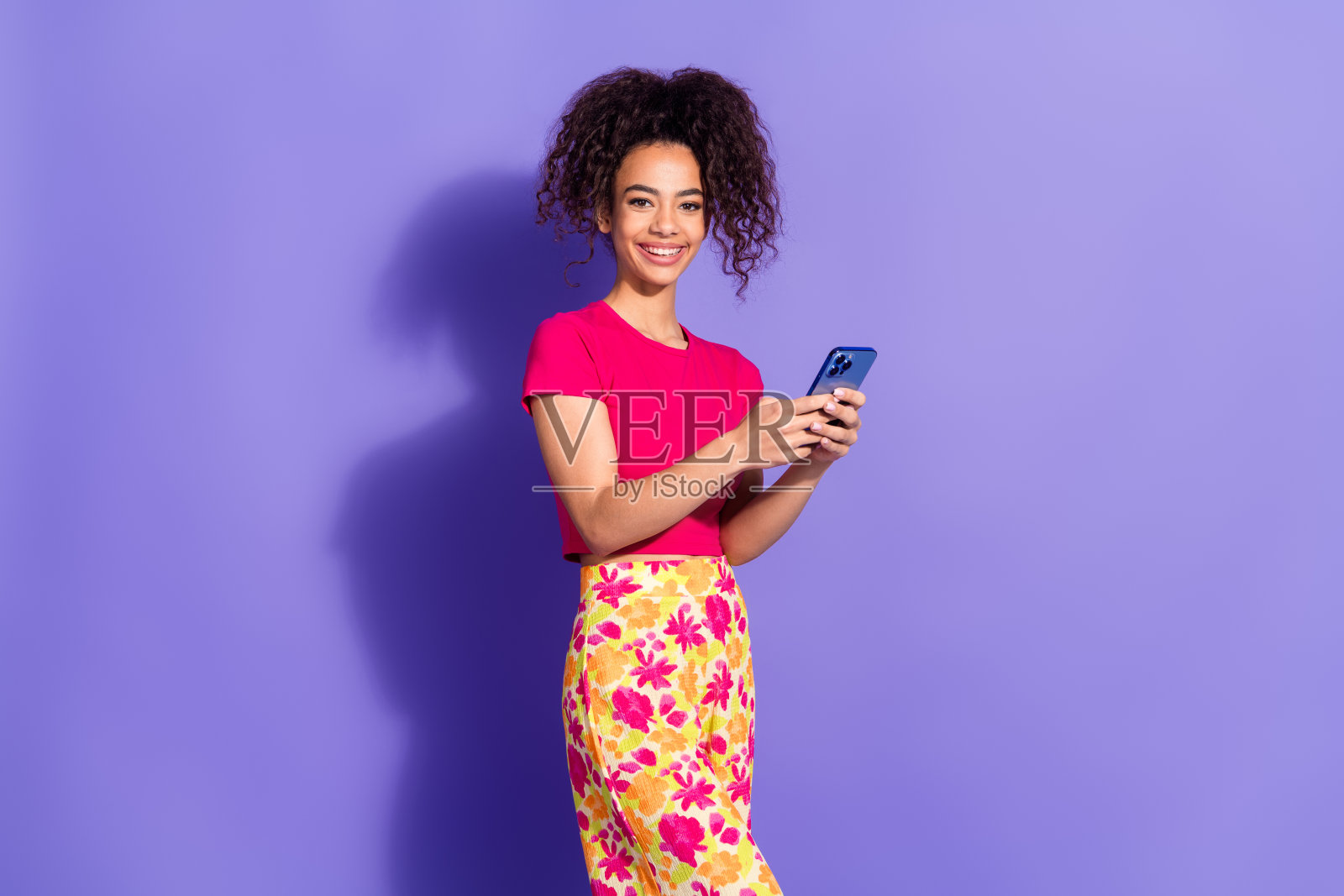 迷人积极的女性穿着粉色上衣,使用现代设备,背景为空白的紫色。照片摄影图片