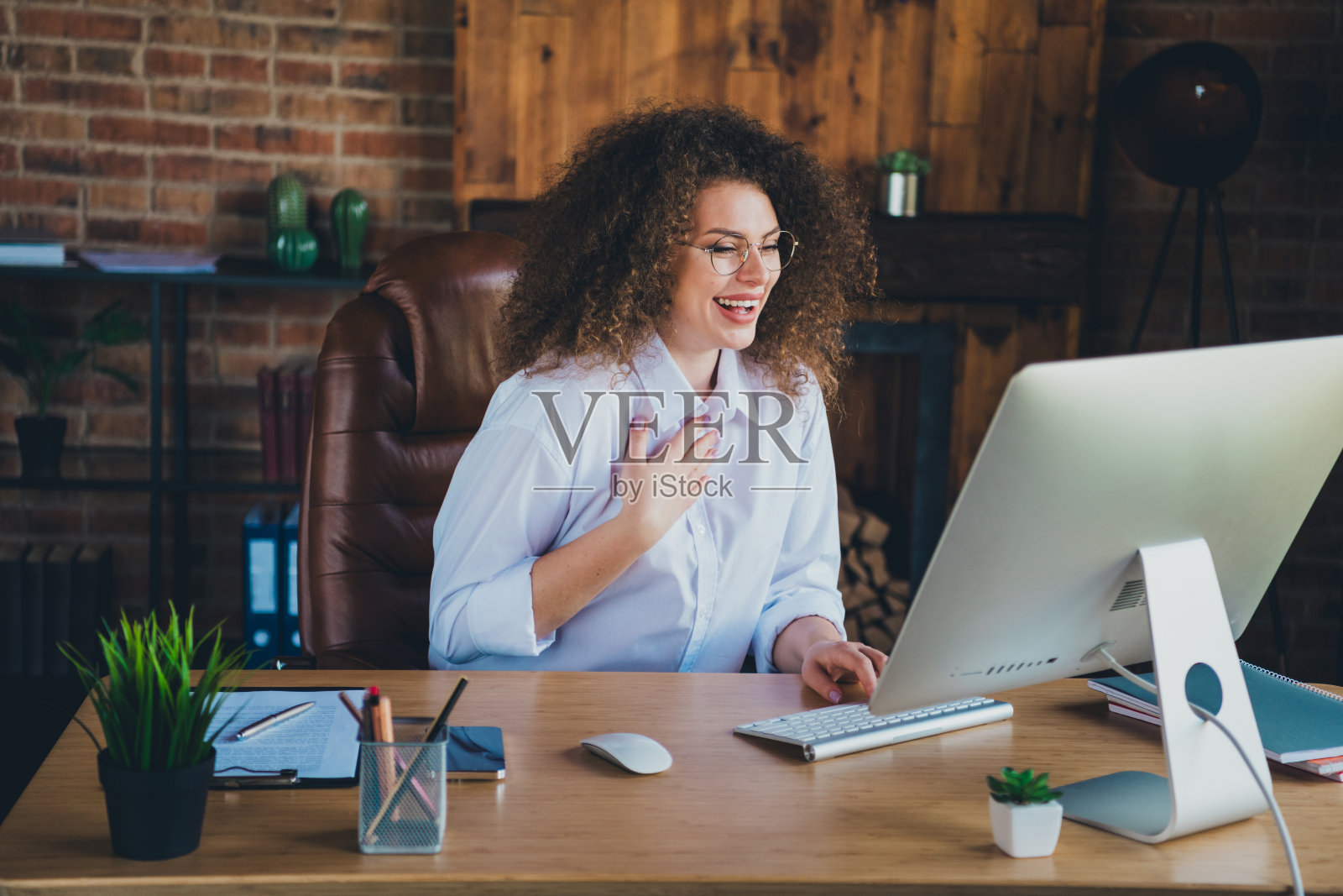 吸引人的卷发年轻女性在现代办公室的商务顾问室内进行电脑视频通话,穿着正式服装。照片摄影图片