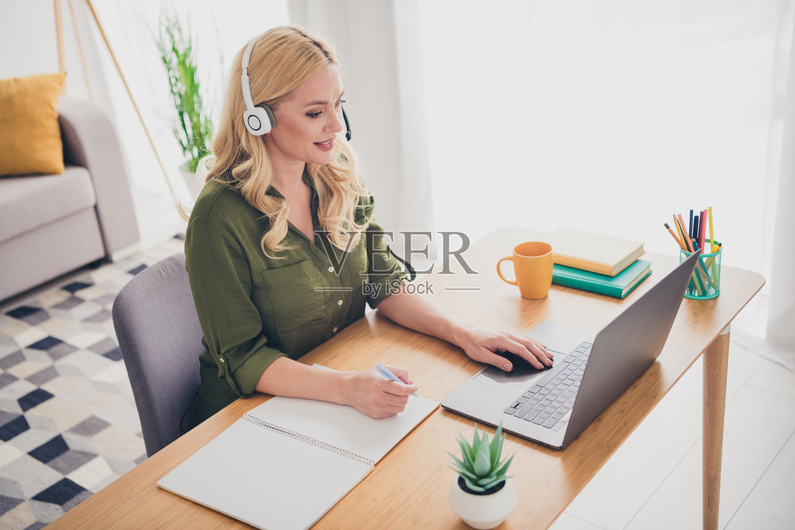 积极的女招聘者穿着衬衫,佩戴耳机,在室内工作场所的公寓中使用通讯设备。照片摄影图片