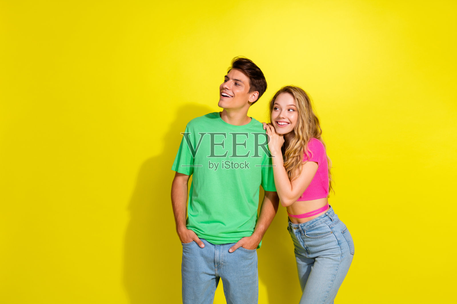 两位年轻伙伴穿着T恤,拥抱着看向空旷的空间,背景为鲜艳的黄色。照片摄影图片