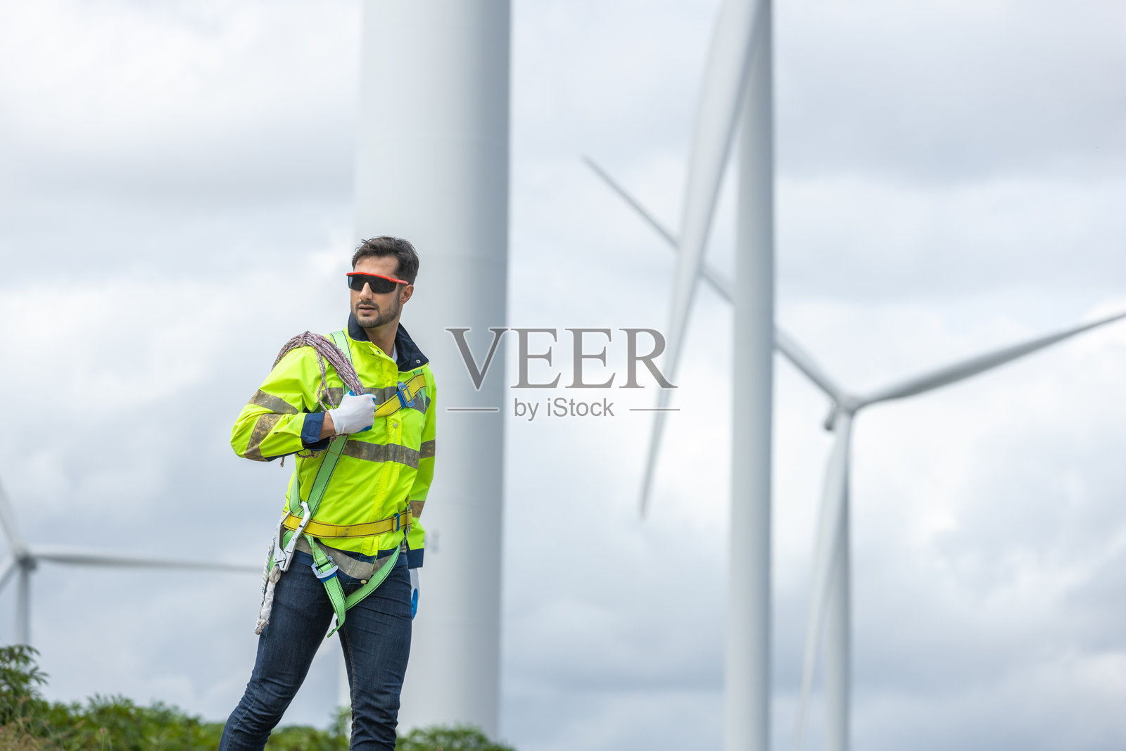 工程师们手持工具箱和绳索,在风力涡轮机上进行维护工作。可再生能源风力涡轮机。技术保护环境,减少全球变暖问题。照片摄影图片