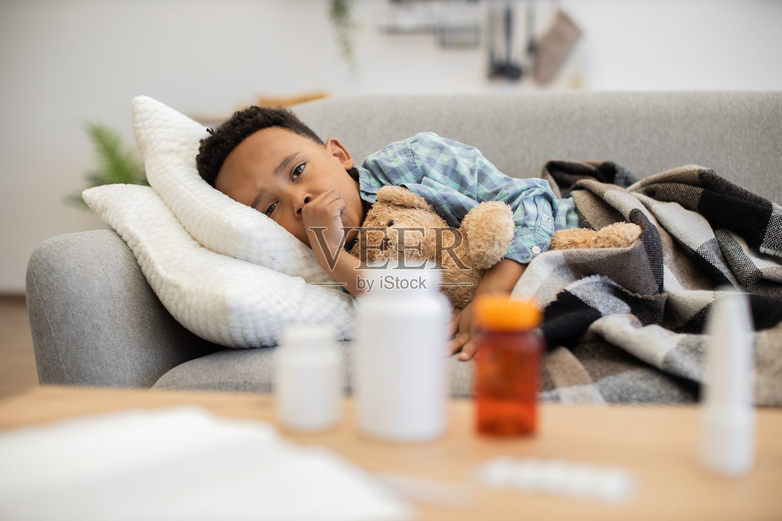生病的小男孩在沙发上与泰迪熊一起休息照片摄影图片