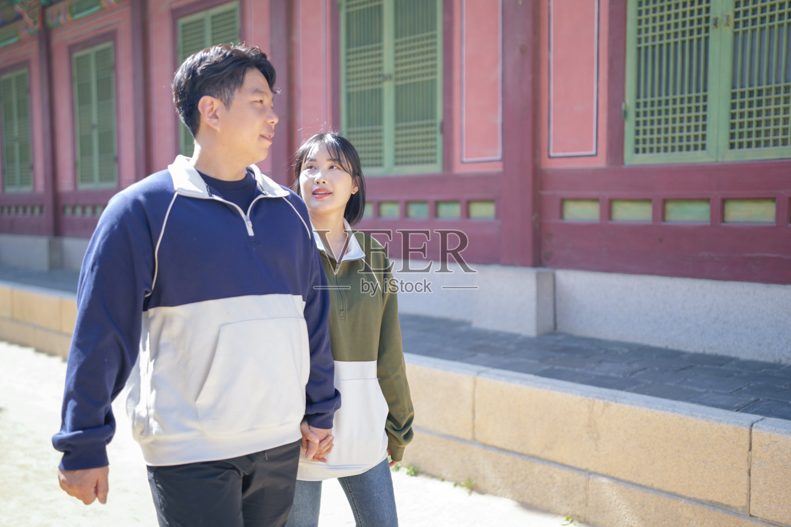 一对韩国情侣,一名30多岁的男性和一名20多岁的女性,身穿韩服,和谐地走过韩国首尔的一座历史建筑。照片摄影图片