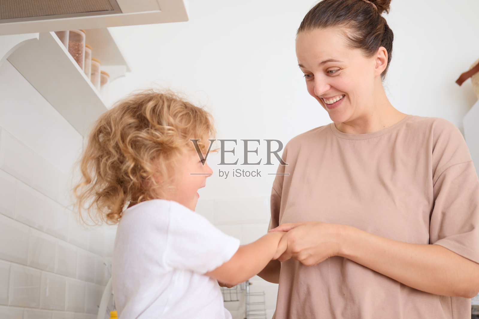 有趣的母亲和孩子在厨房里愉快地交流,开心地一起笑,享受家庭快乐时光。照片摄影图片