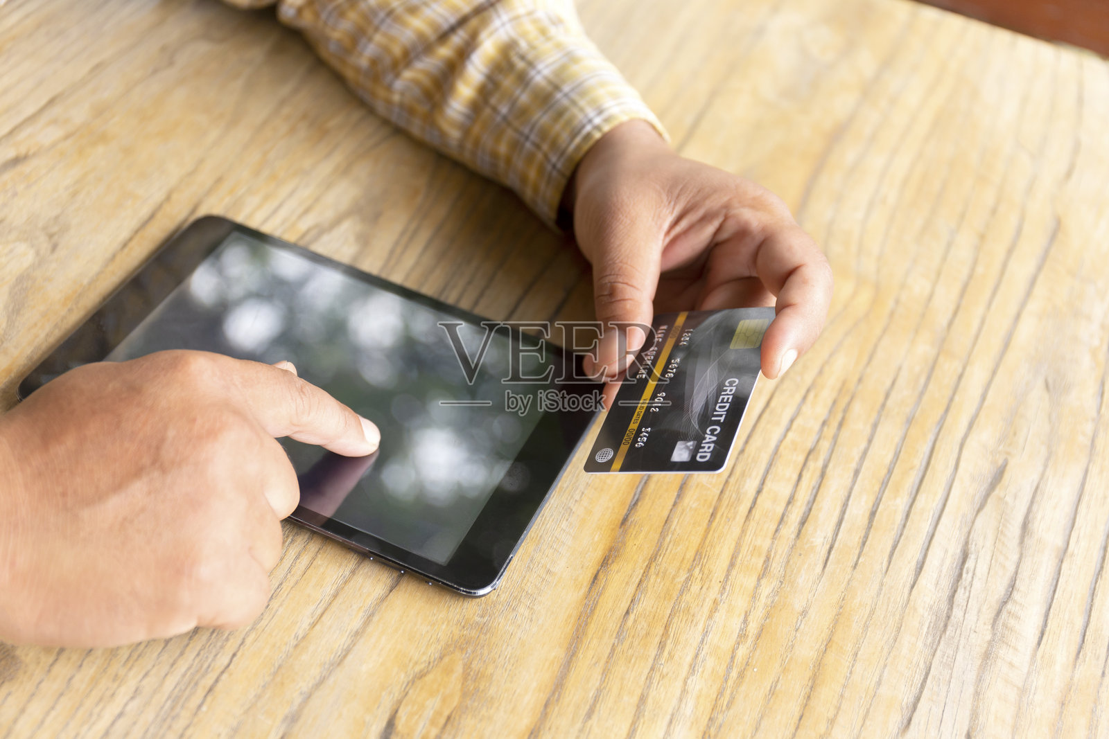 一个人用手握着信用卡,正在桌子上使用平板电脑。照片摄影图片