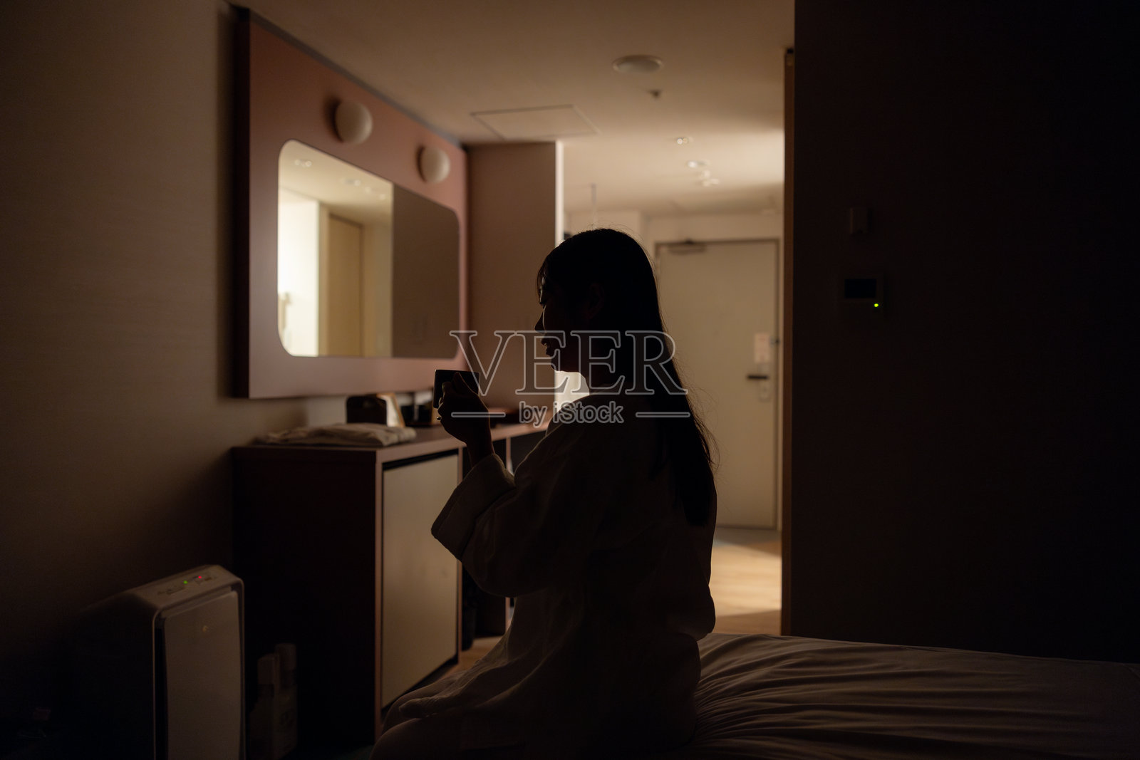 夜晚酒店房间里,穿着睡衣的女性剪影手持咖啡杯照片摄影图片