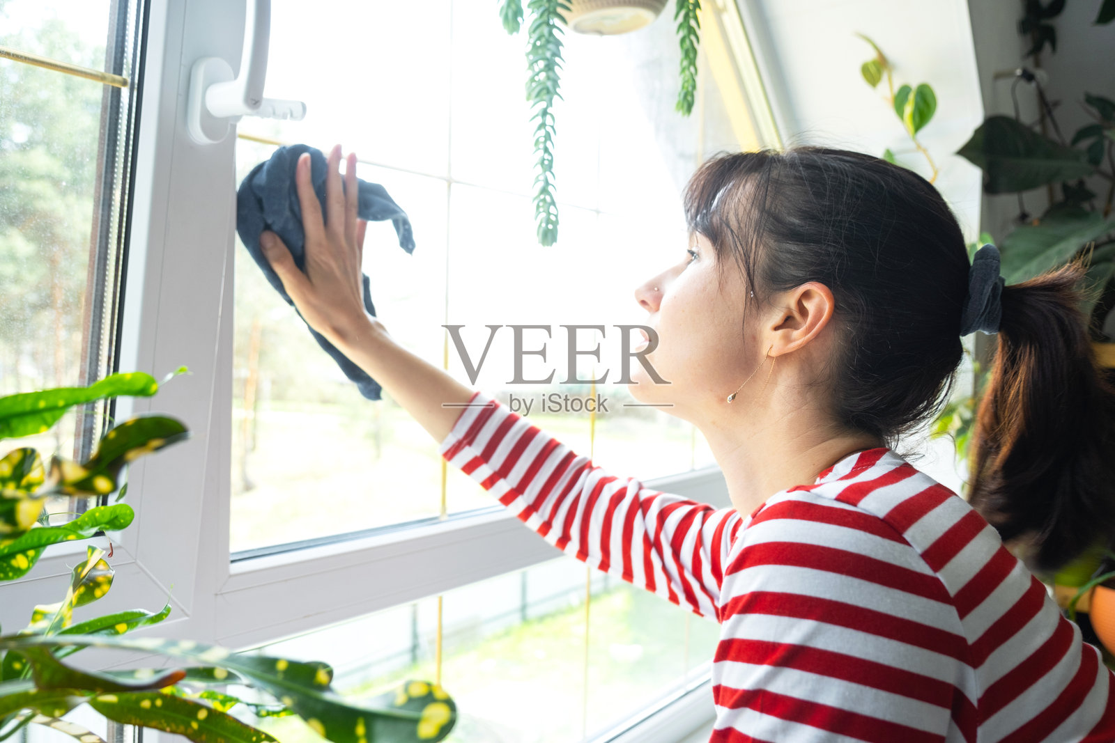 女人在室内用抹布和拖把手动清洗窗户,窗台上摆放着家居植物,阁楼在背景中。春季恢复秩序和清洁,清洁服务。照片摄影图片