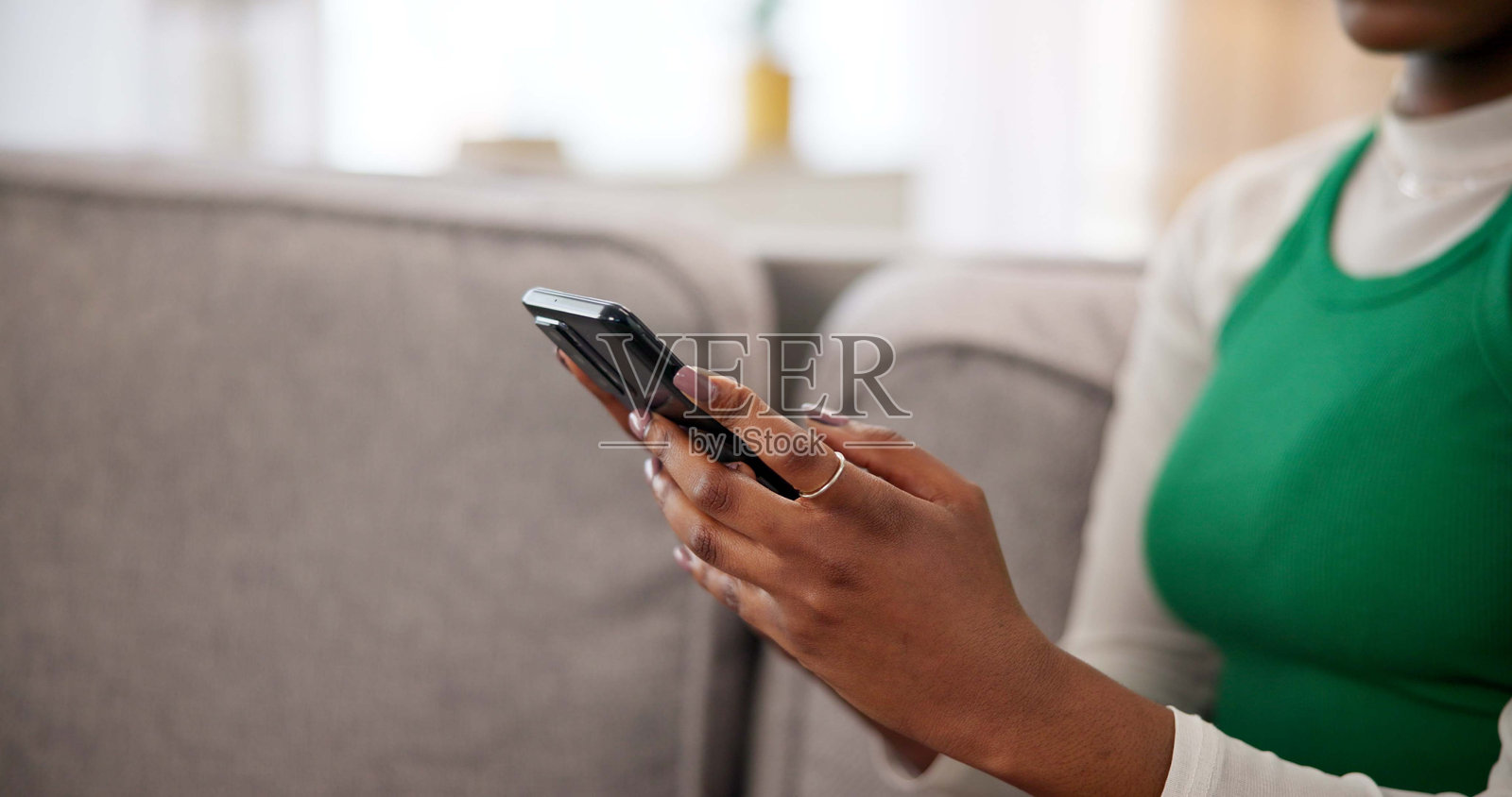 女人坐在沙发上,手中拿着智能手机,正在家中客厅或公寓里进行互联网交流。她在社交媒体上浏览视频,作为学生的人正在在线聊天。照片摄影图片