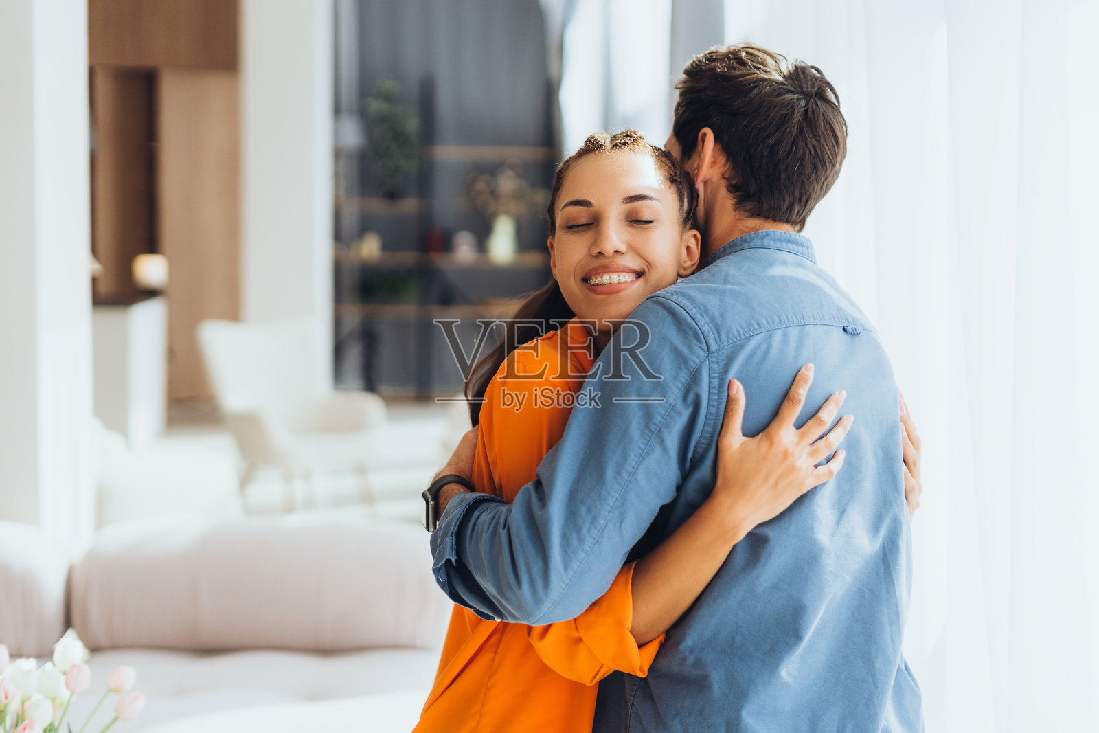 一对积极微笑的拉丁夫妇在现代家居环境中相拥而立。照片摄影图片