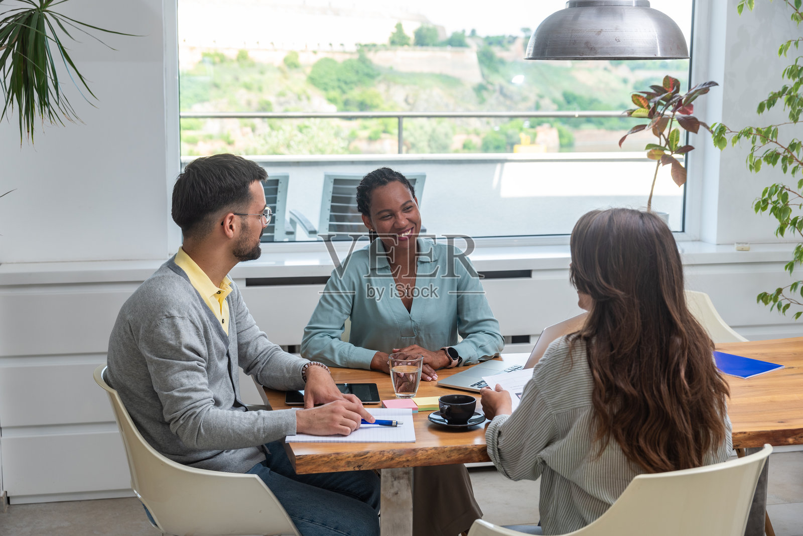 一群多元化的年轻商务人士在现代小办公室的会议中,微笑着一起使用笔记本电脑。男商人和女商人正在合作开发廉价住房的新创新项目。照片摄影图片