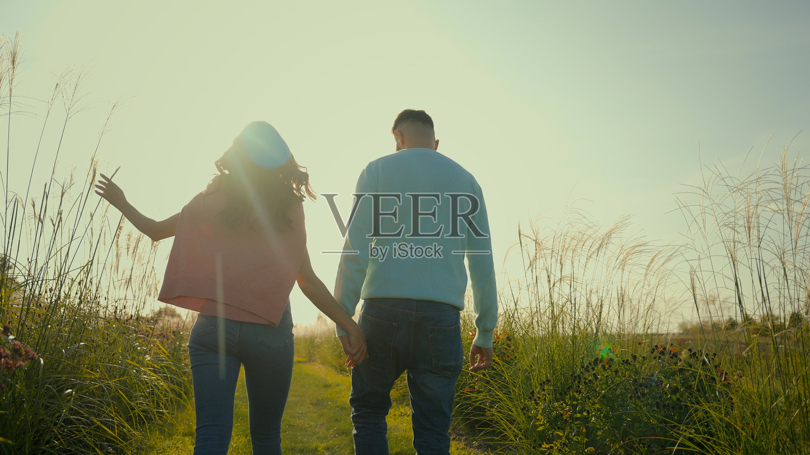 背影可爱的白人情侣,女性女孩与男性男友手牵手在阳光明媚的乡村田野散步,交谈享受假期。照片摄影图片