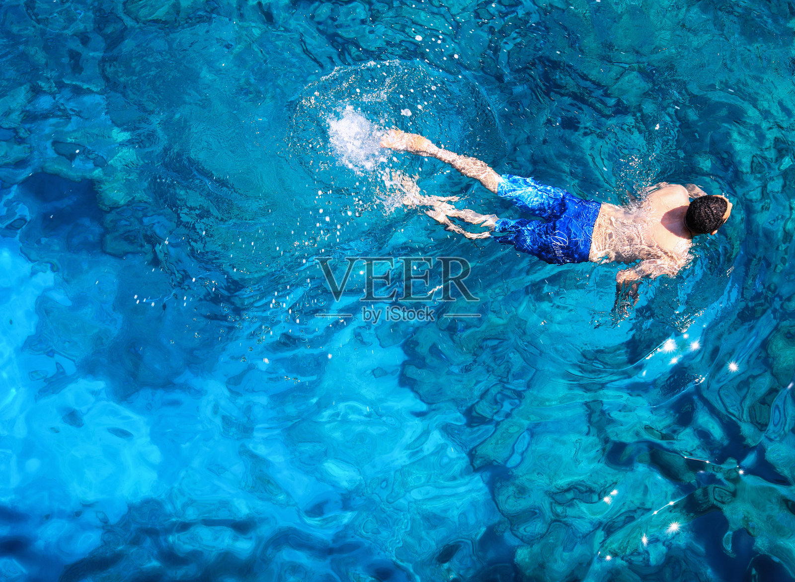 阳光明媚的日子里,俯视一名赤裸上身的男子在蓝色海洋中游泳照片摄影图片