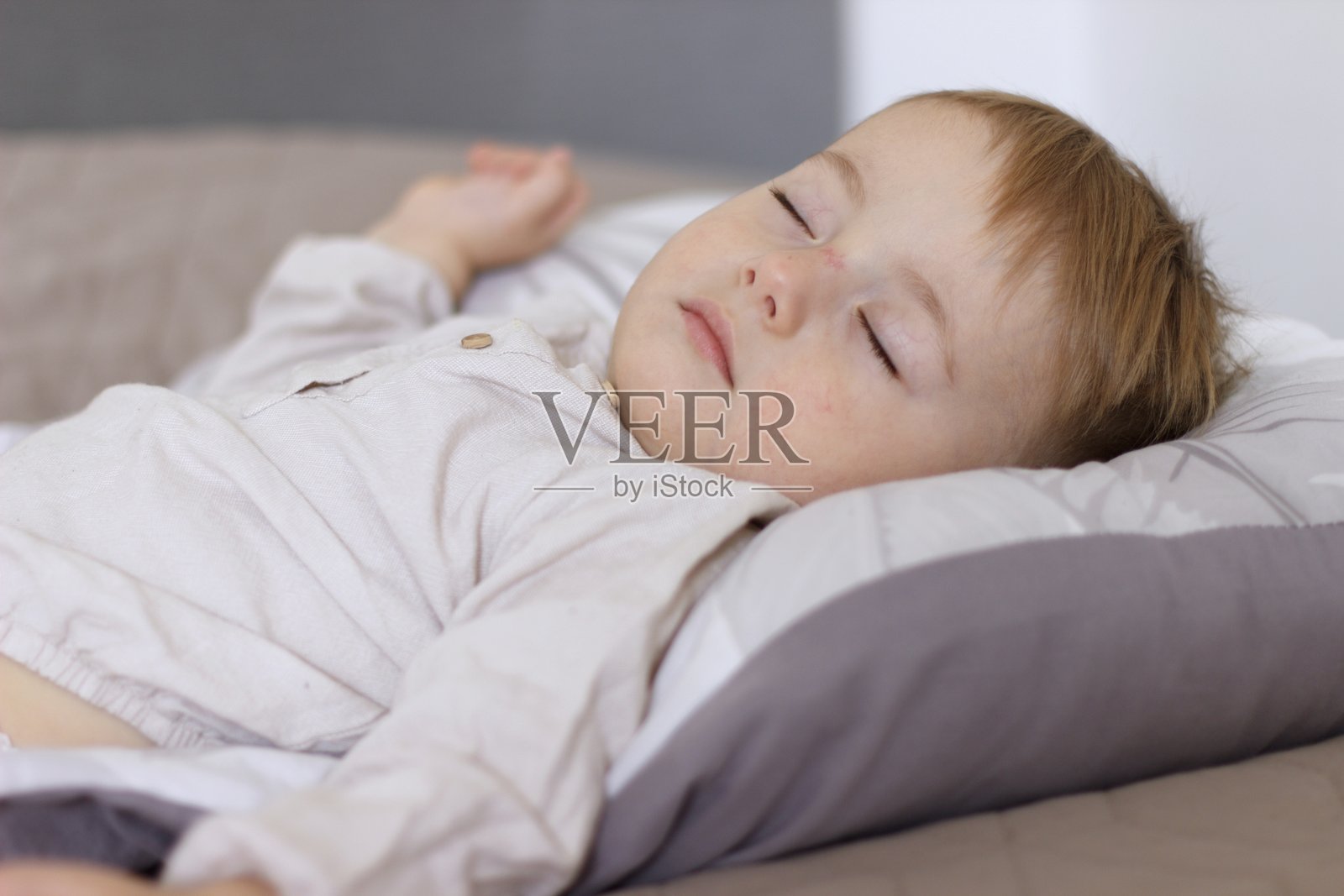 白天,孩子在睡觉。宝宝在做白日梦,他穿着米色衬衫,躺在一张浅色的床上。照片摄影图片
