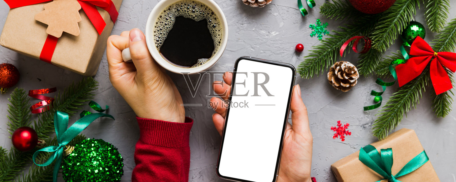 女性手持智能手机和热咖啡杯的俯视图。彩色背景上的圣诞装饰。照片摄影图片
