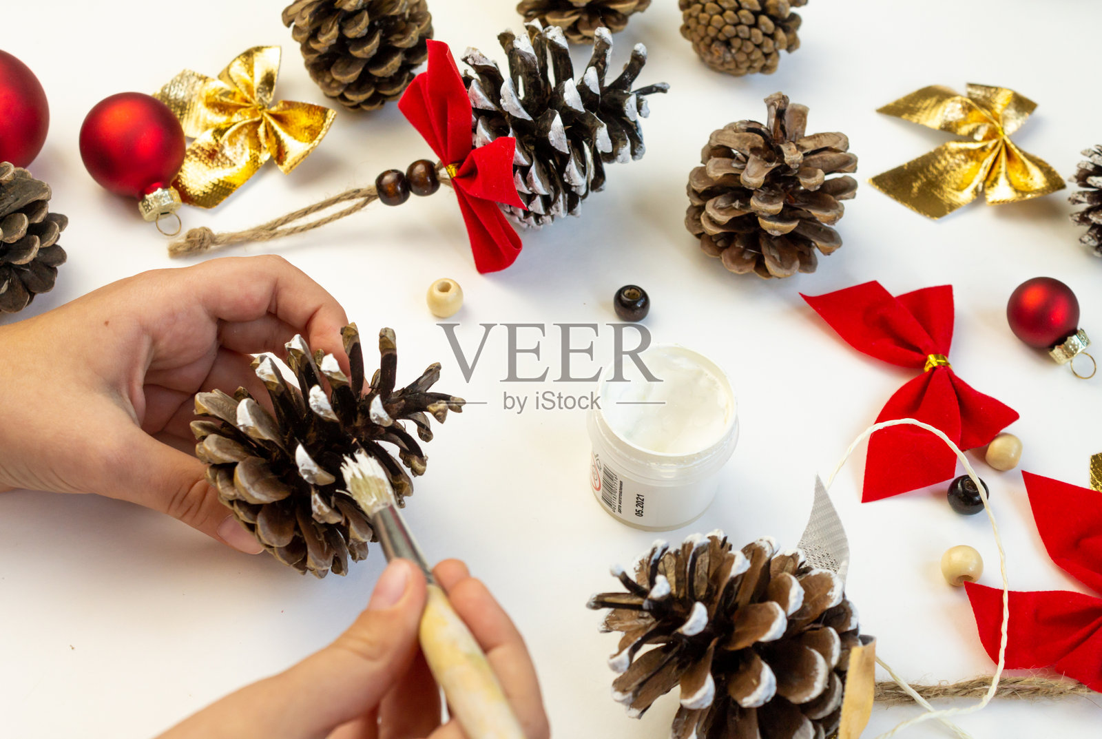 用松 cones 制作的圣诞树玩具。孩子们的创造力。手部特写,正在用白色颜料涂抹松 cones。照片摄影图片