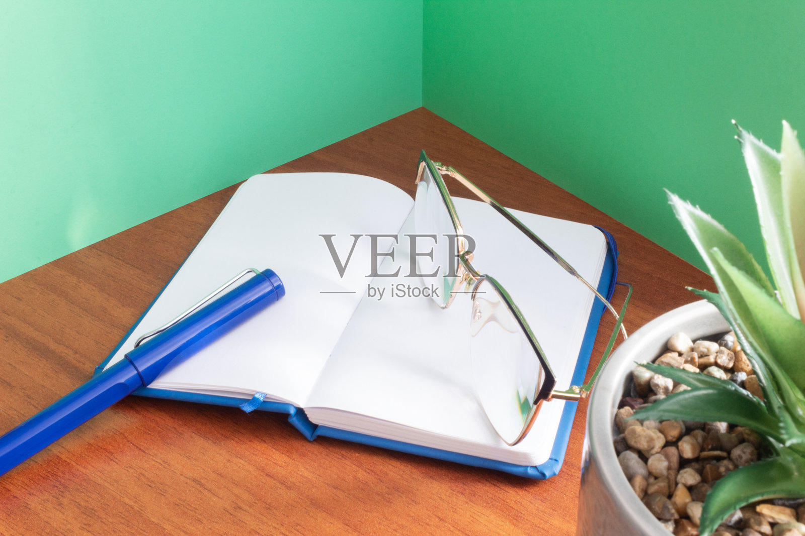 一支优雅的钢笔和眼镜放在一本打开的空白笔记本上,周围是绿色的墙壁。工作空间。手写。照片摄影图片