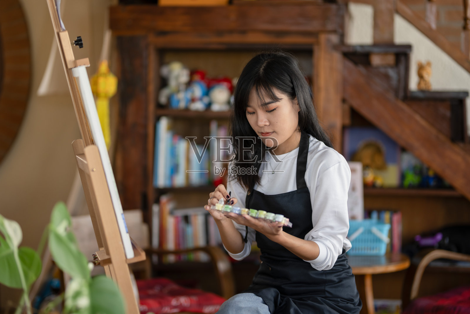 一位微笑的年轻女性在温馨舒适的艺术工作室中享受绘制色彩斑斓的画布。照片摄影图片