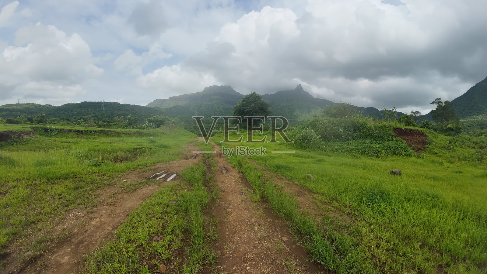 一条泥泞的小路穿过郁郁葱葱的草地,映衬在多云的天空下。照片摄影图片