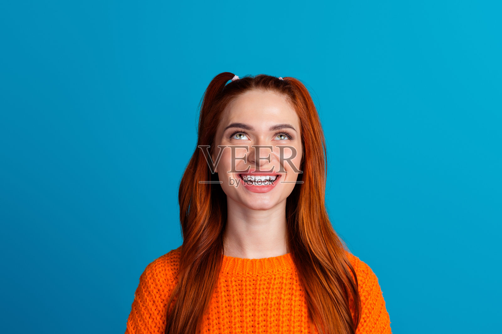 漂亮年轻女孩的照片肖像,仰望空旷的空间,穿着时尚的橙色针织服装,背景为蓝色。照片摄影图片