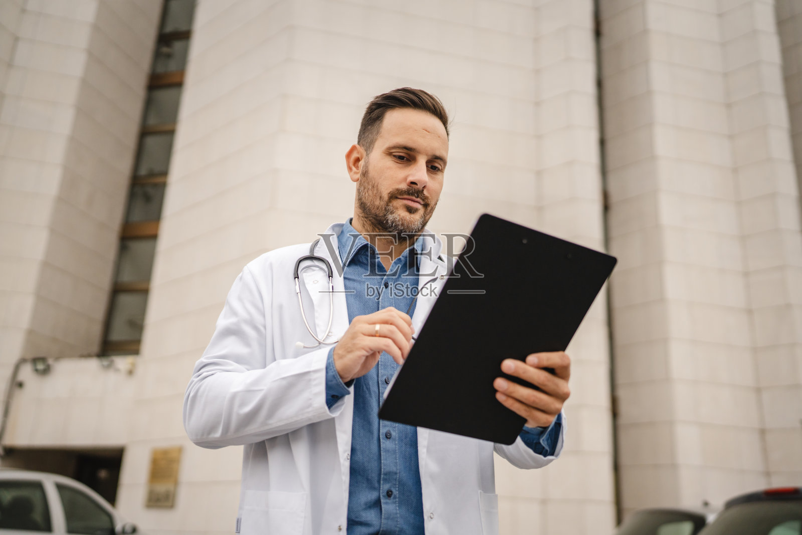 男医生站在建筑前查看夹板上的信息照片摄影图片