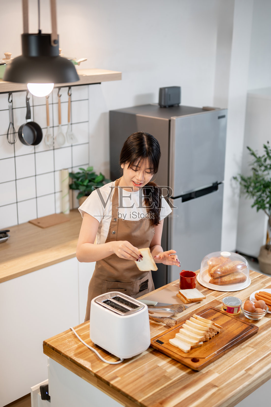 一位漂亮的亚洲女性正在厨房用烤面包机烤面包,为自己准备早餐。照片摄影图片