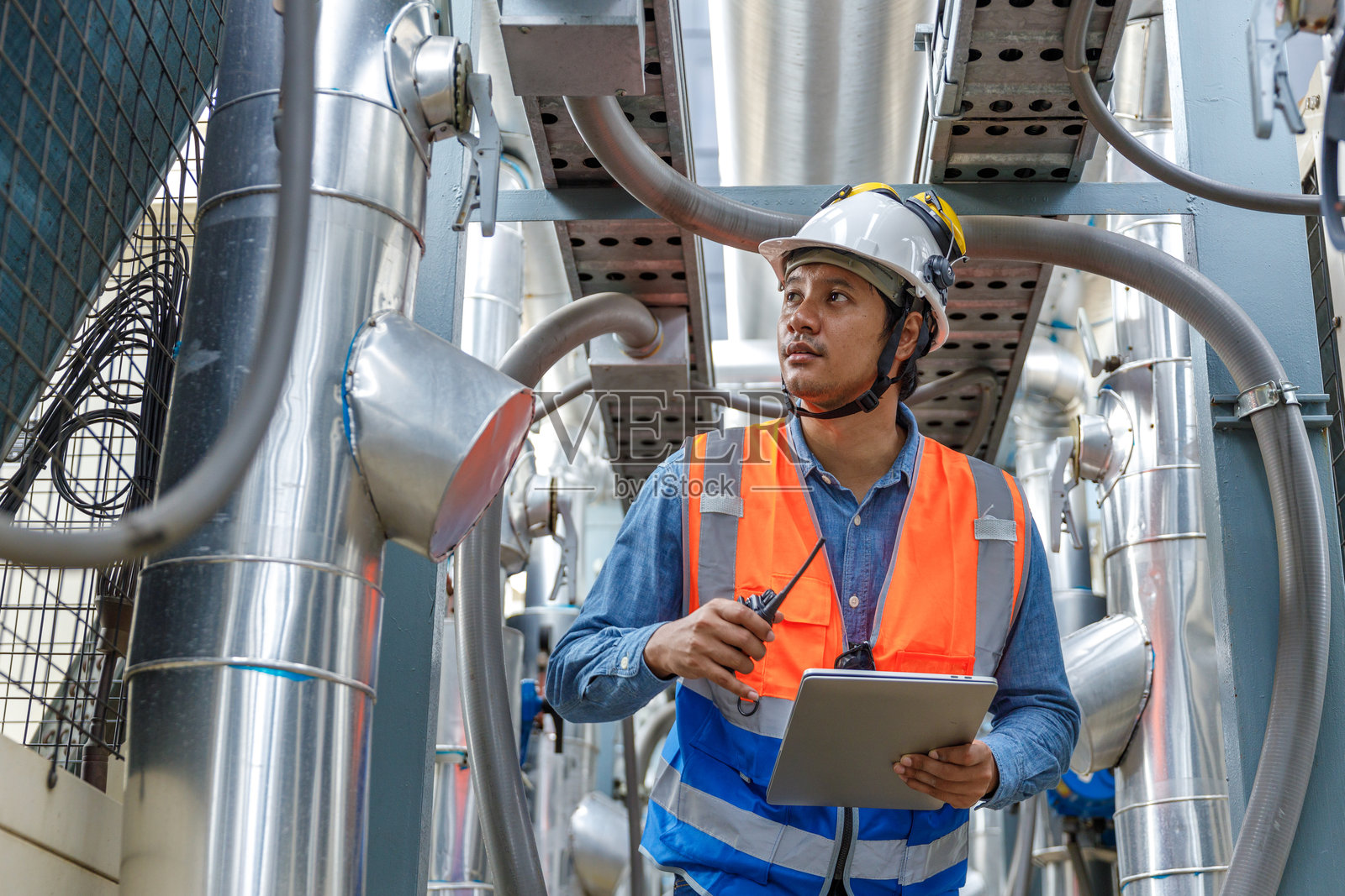 男性操作员使用对讲机和笔记本电脑检查工业建筑的冷却空气管道质量。工程师正在进行供暖、通风和空调系统的工作。照片摄影图片