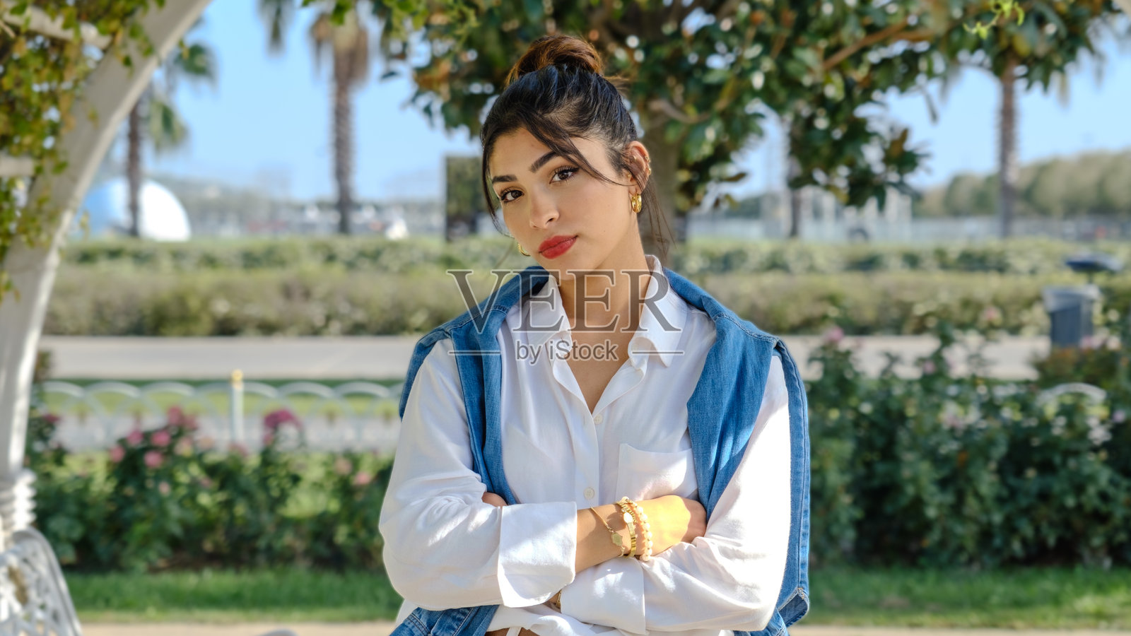 一位年轻的棕发女商人在春天的树木繁茂的公园里,面向镜头,面部表情显示出她感到无聊。照片摄影图片