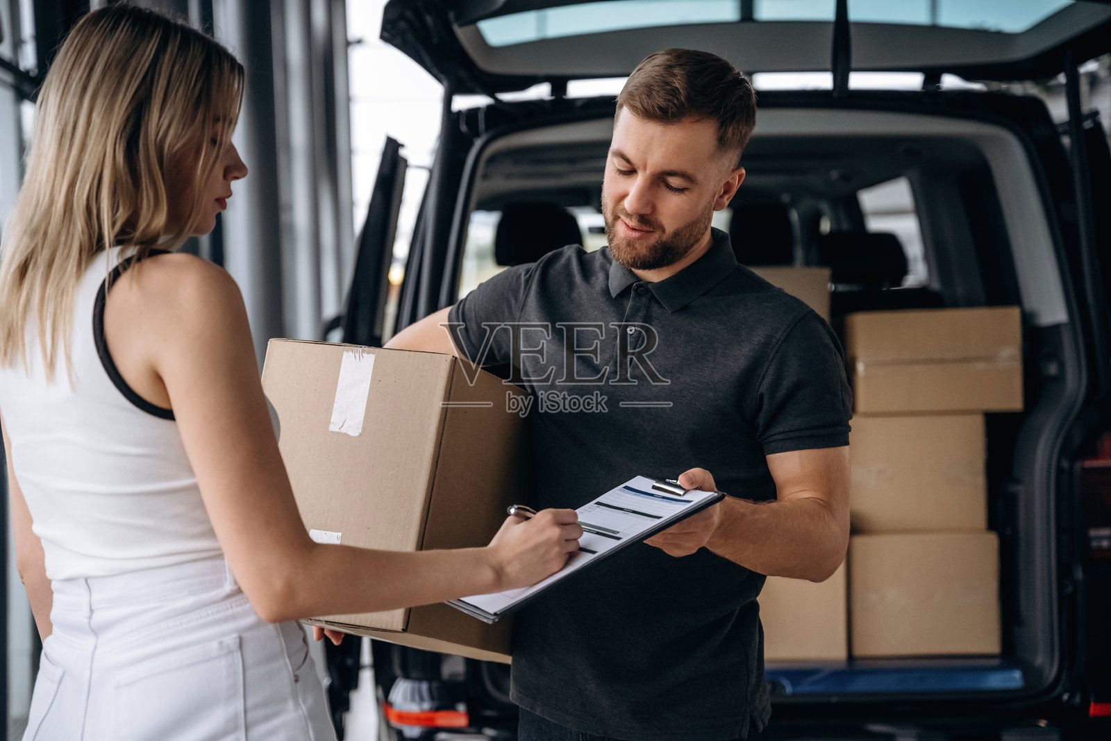 专业服务。女性正在从送货员那里接收订单,旁边有一辆车。照片摄影图片