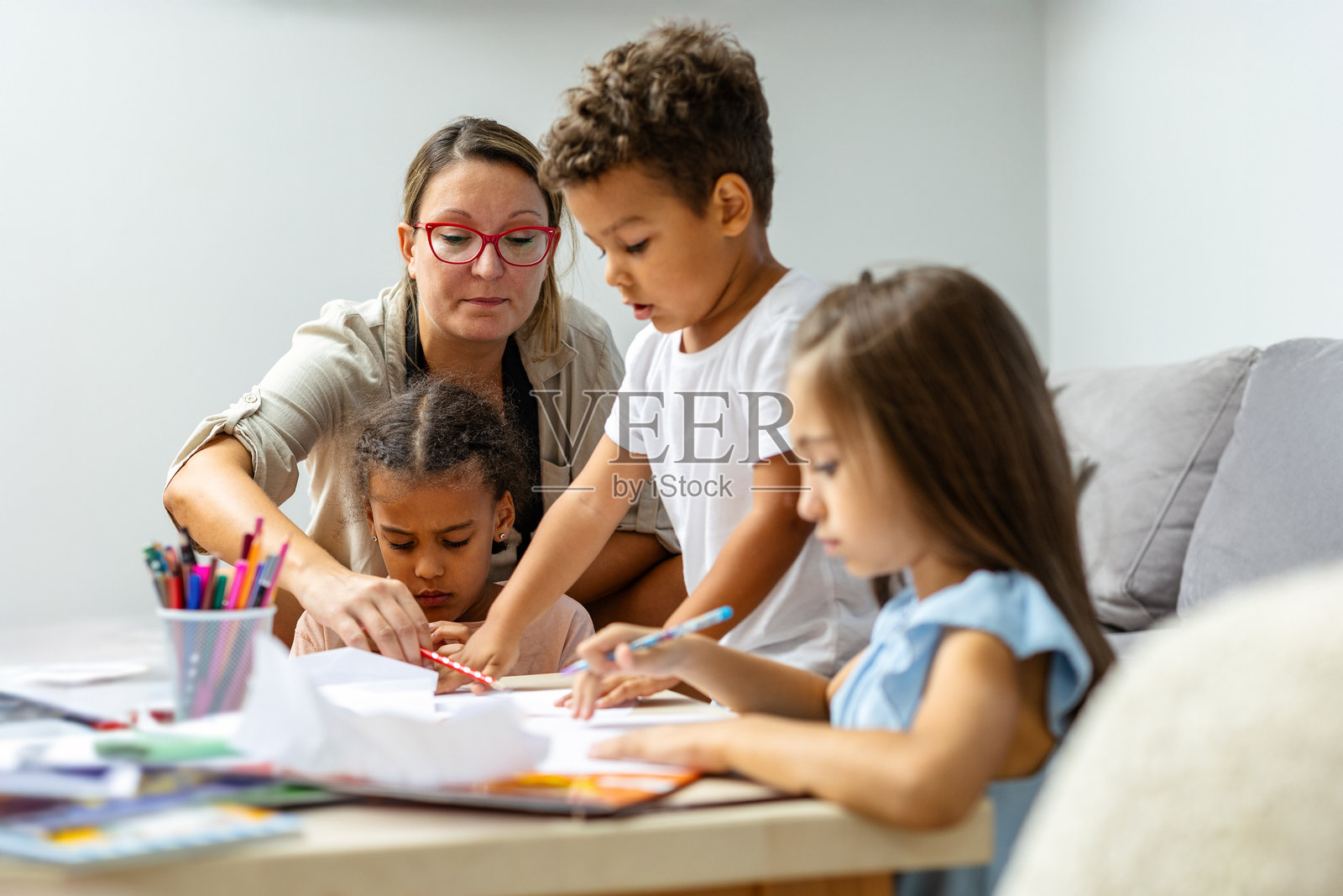 女人在温馨的家中帮助孩子们画画。照片摄影图片