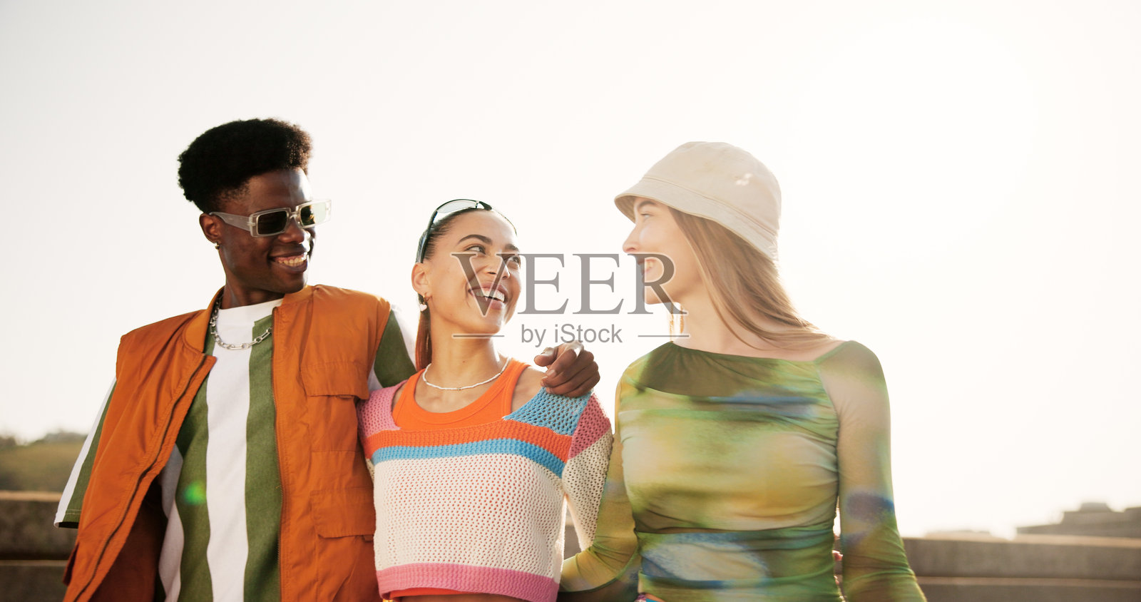 城市中,朋友们穿着时尚街头服饰,互相拥抱,展现出年轻一代的风格。多样性,男女欢笑着,穿着夏季服装,戴着太阳镜,享受户外重聚的快乐。照片摄影图片