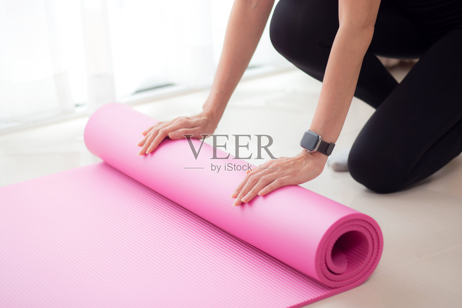 年轻女性的手特写,正在地板上卷起瑜伽垫,为冥想和锻炼做准备,进行健康活动和爱好的瑜伽训练。照片摄影图片