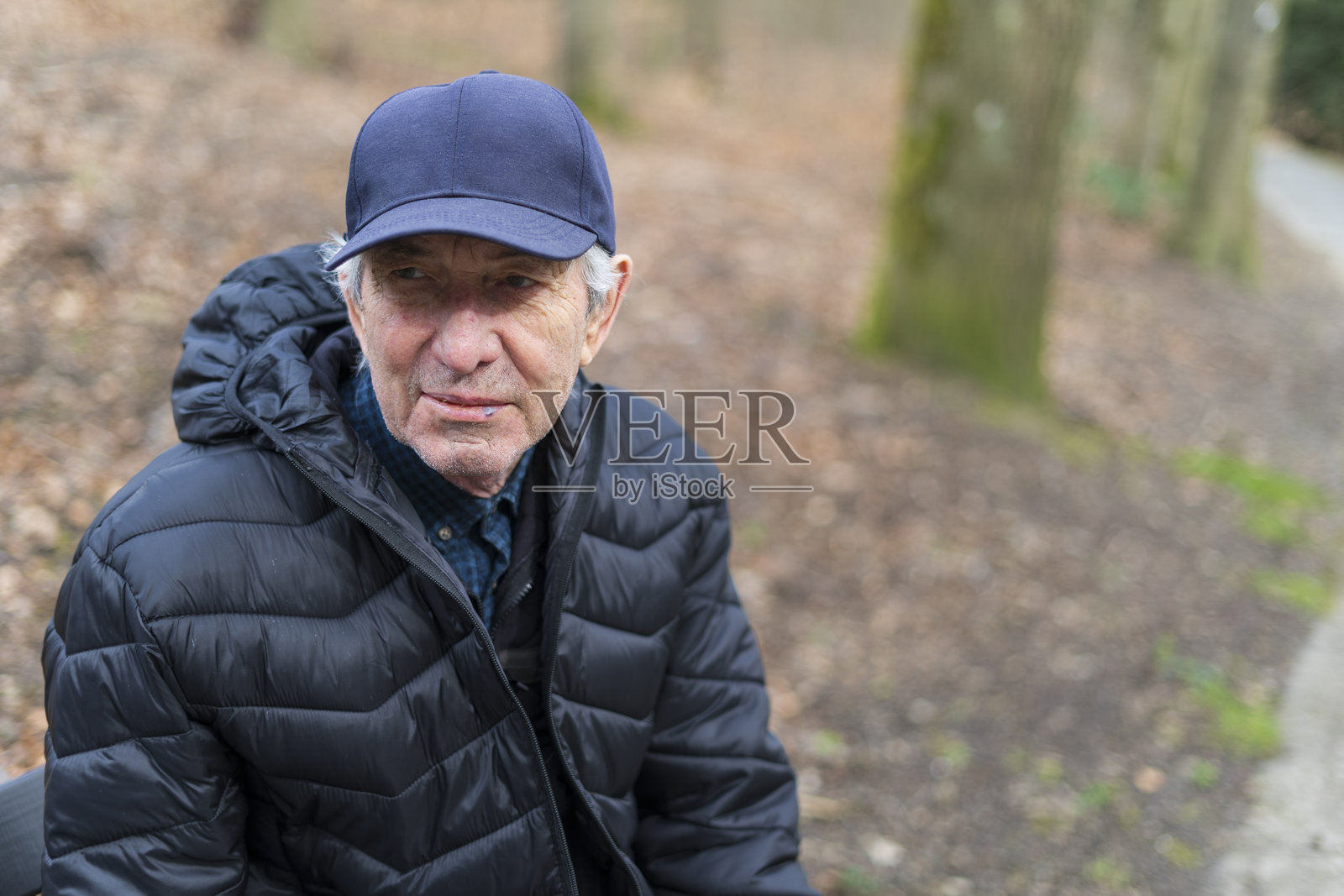 一位戴着帽子的老人坐在秋天公园的长椅上。艰难老年生活的概念照片摄影图片