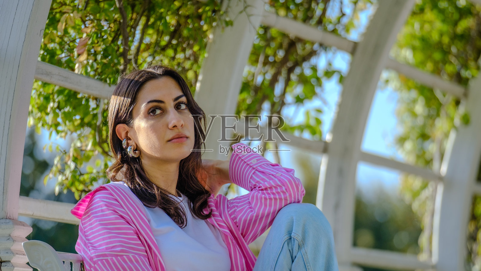 一位美丽的年轻棕发女性在阳光明媚的树木繁茂的公园里为镜头摆姿势照片摄影图片